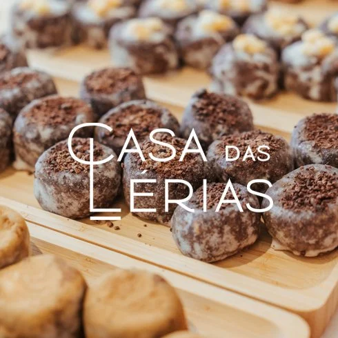 Doces de chocolate polvilhados com açúcar em uma bandeja de madeira com o texto 'Casa das Lérias' em destaque