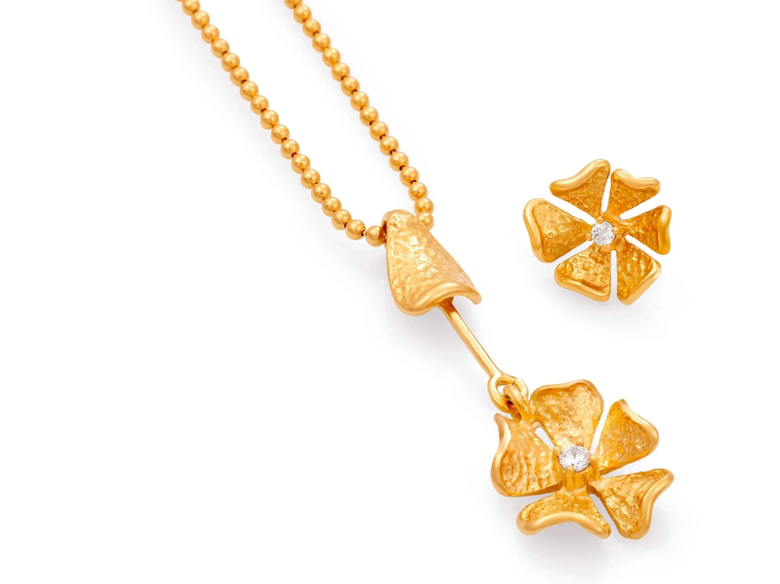 Joia de ouro com colar de bolinhas e dois pingentes em formato de flor, com detalhes texturizados e centro de pedra brilhante.