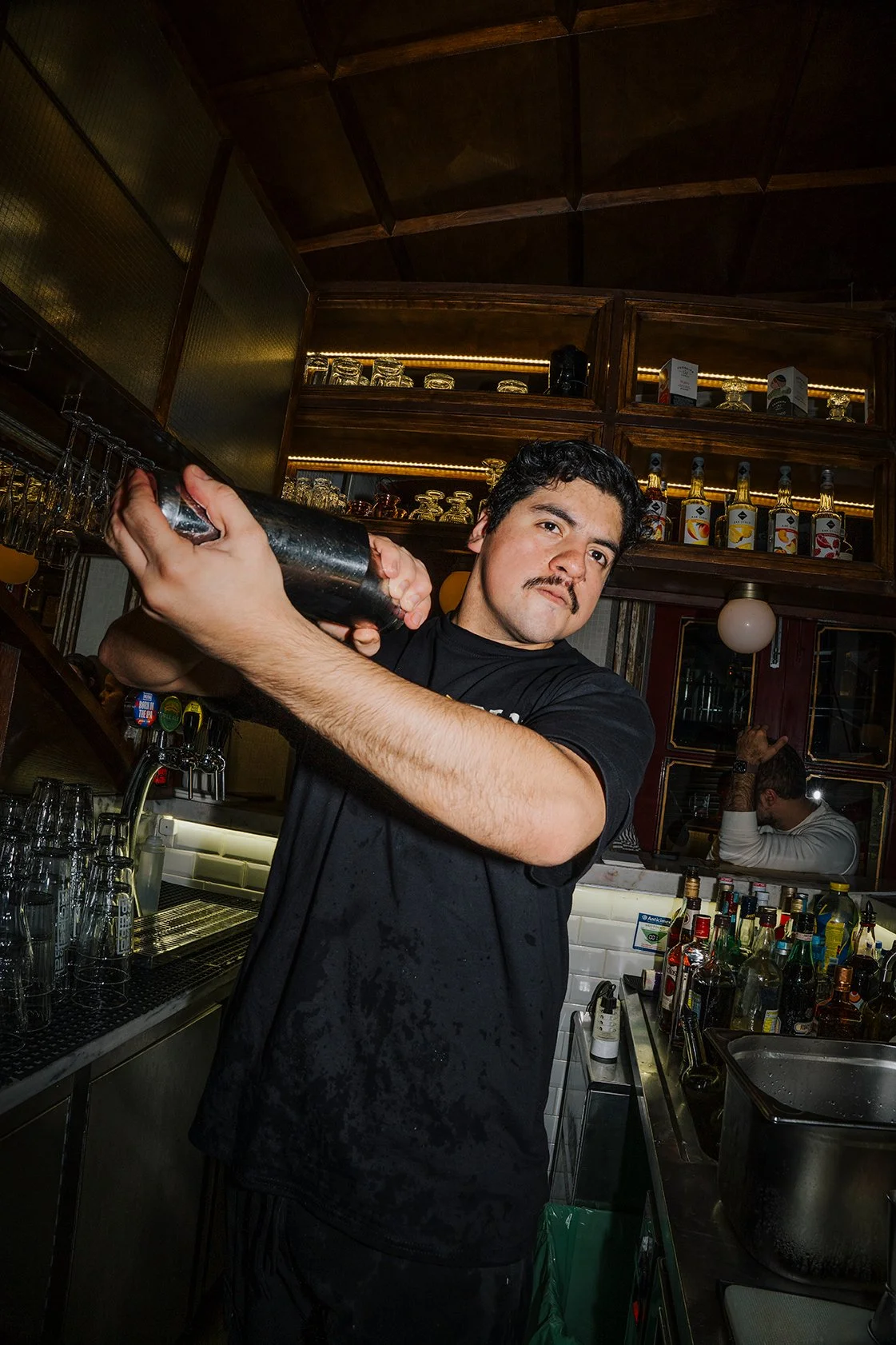 Barman preparando drink em bar com garrafas de álcool ao fundo.