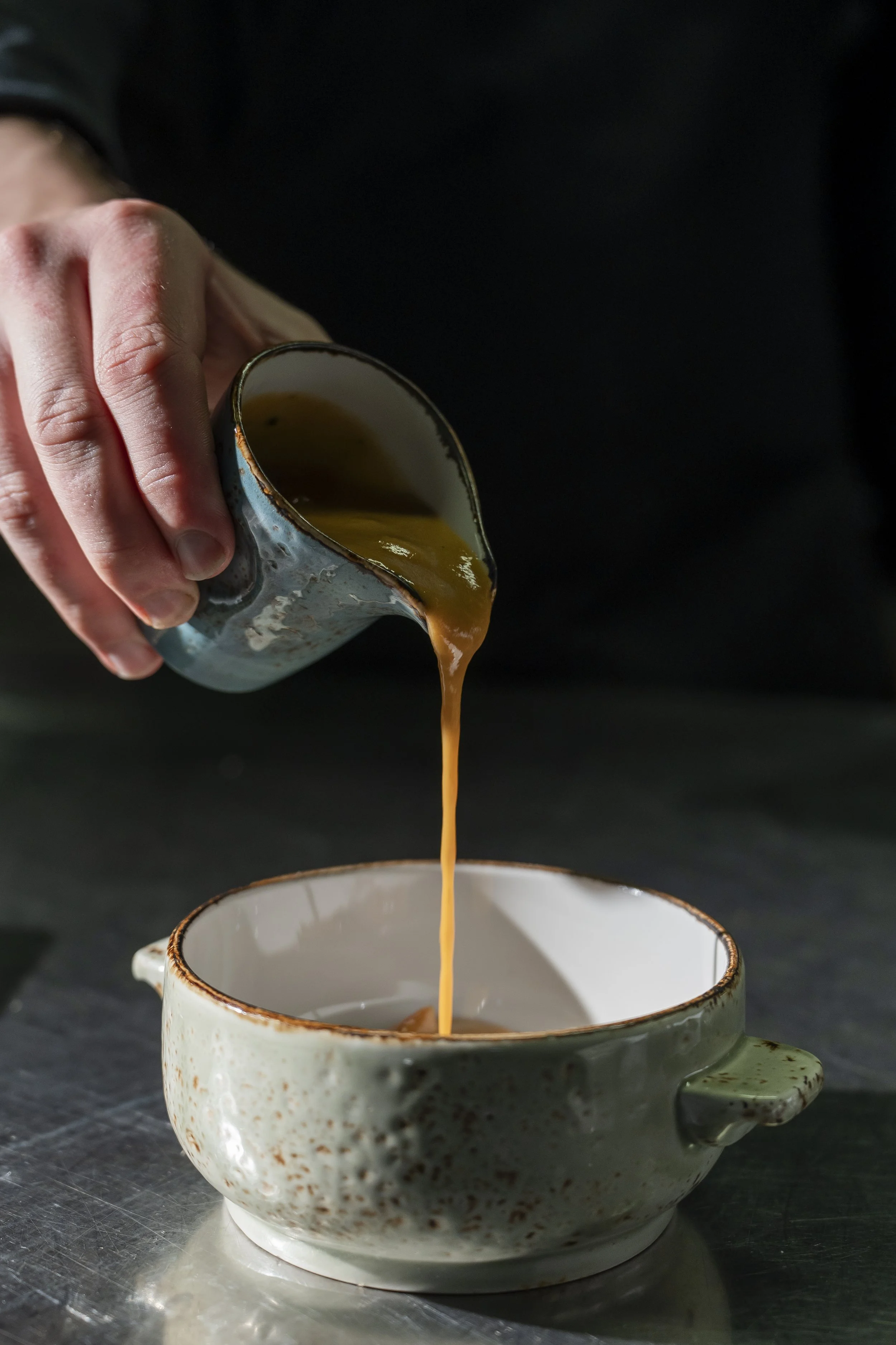 Pessoa despejando café de uma xícara de cerâmica em uma tigela.