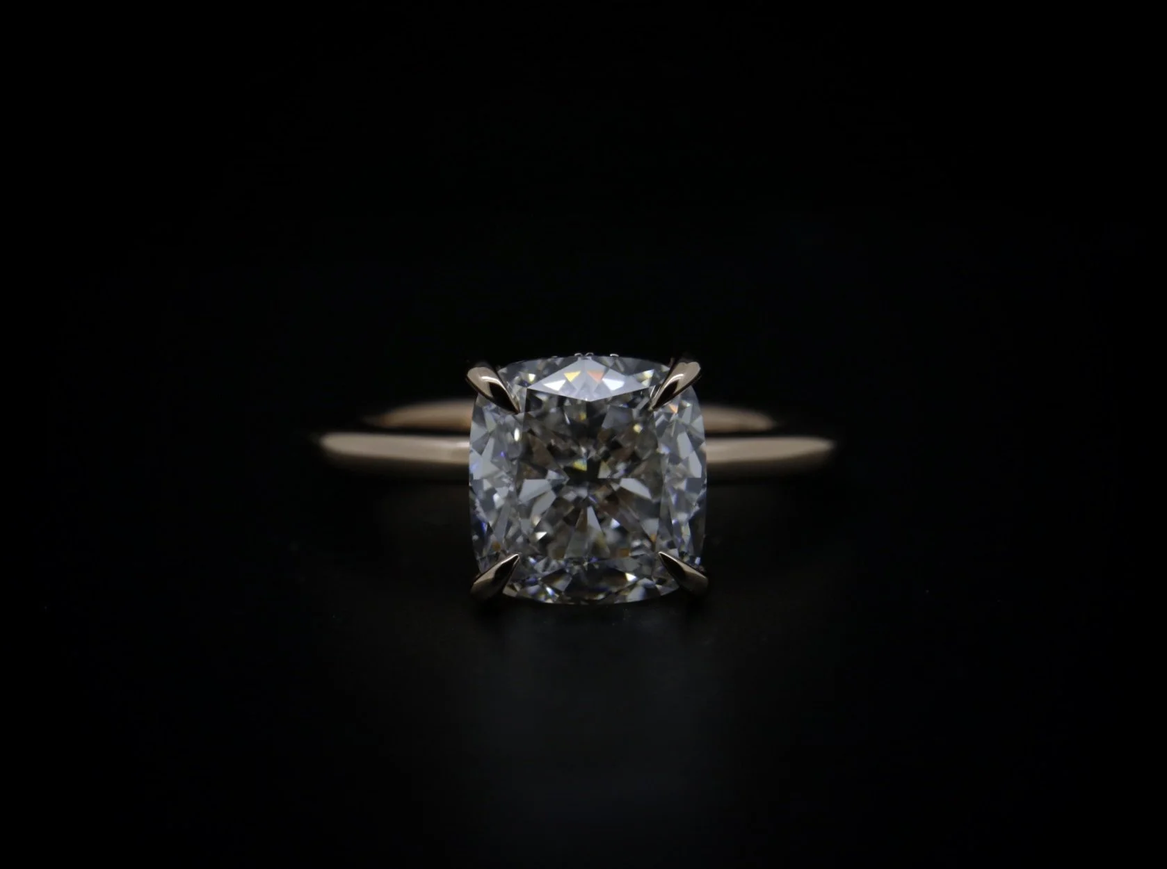A close-up of a diamond ring with a rectangular center diamond in a prong setting, against a dark background.