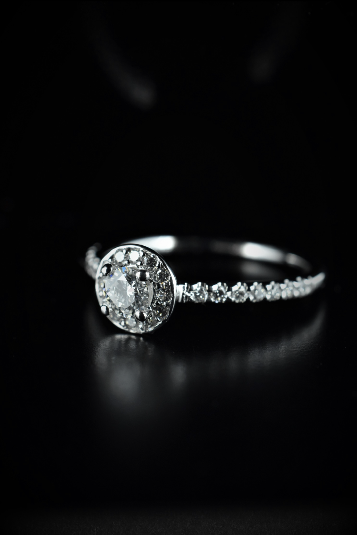A silver ring with a central round diamond surrounded by smaller diamonds, set on a black background.