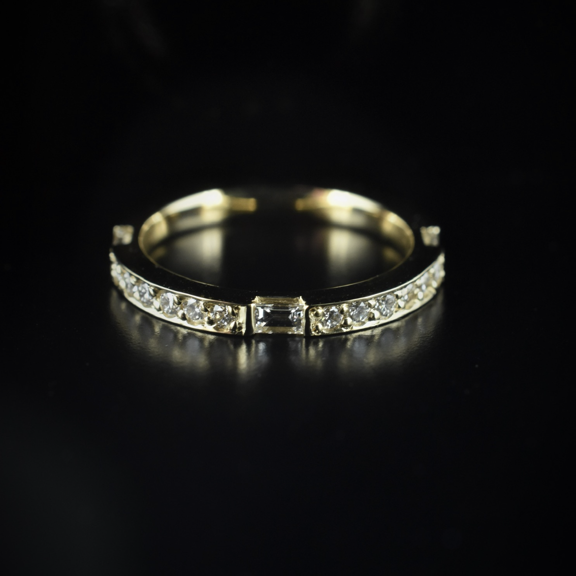 A silver ring with small diamonds along the band and a larger square diamond in the center, set against a black background.