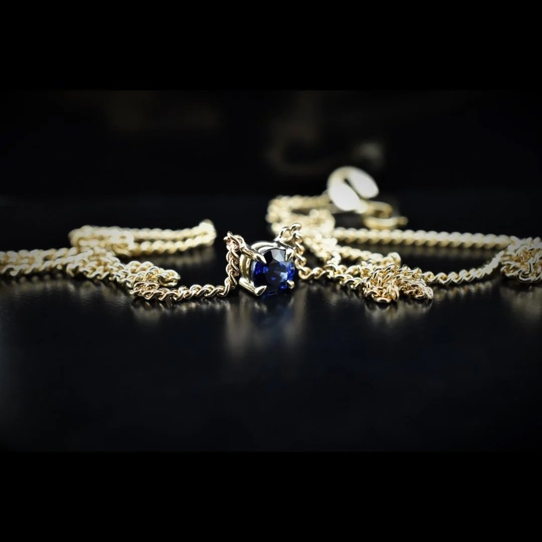 Gold chain necklace with a dark blue gemstone pendant resting on a black surface.