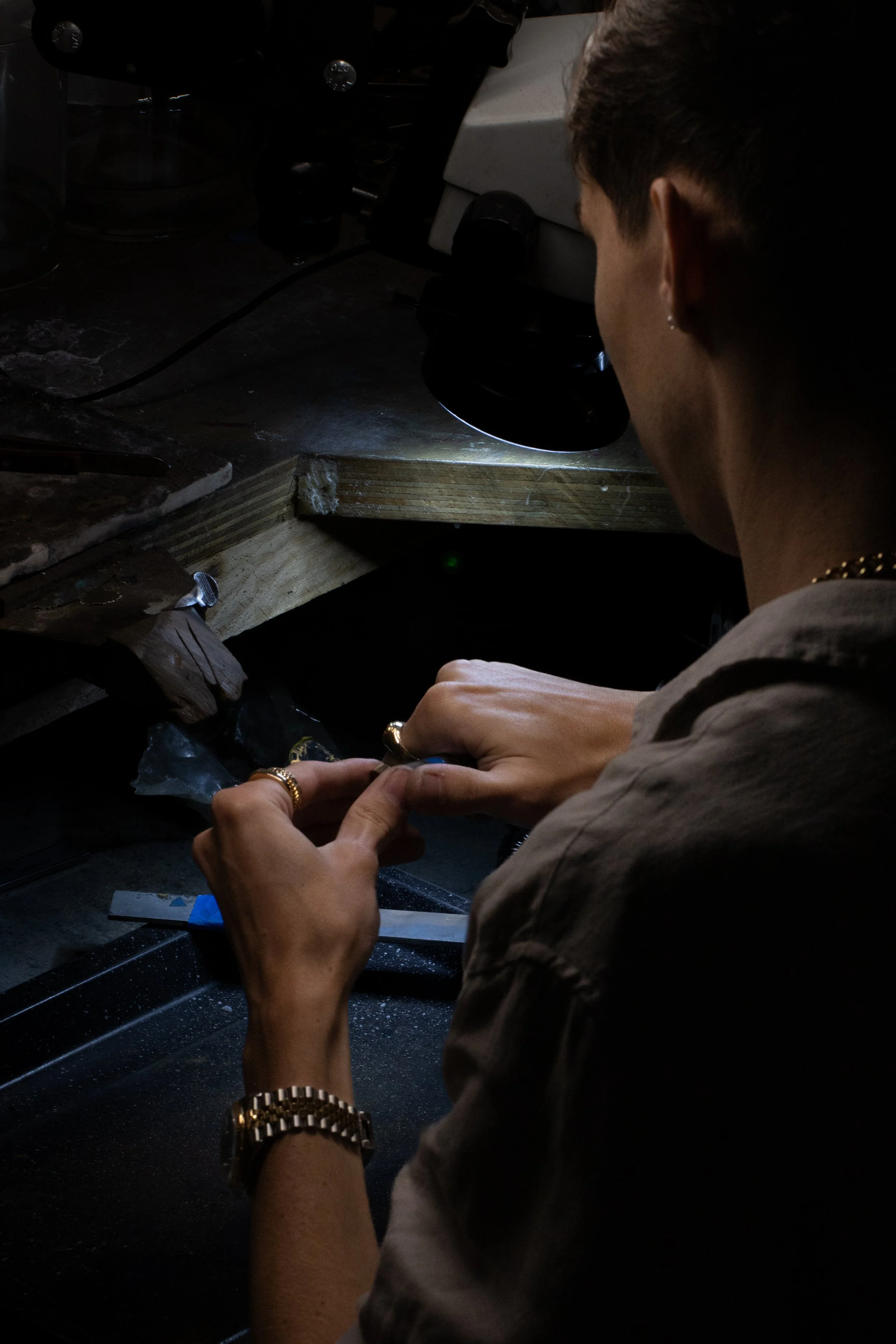 A person working in a dark laboratory, using a microscope and handling a small object.