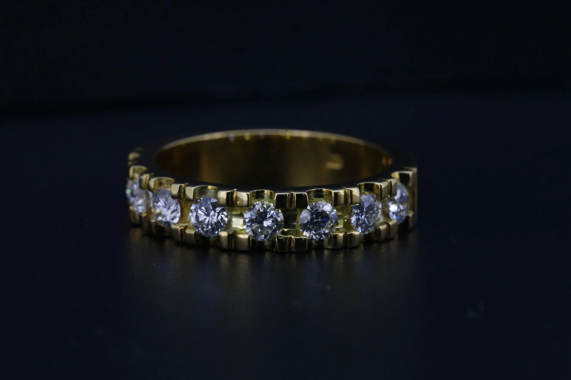Gold ring with embedded round-cut diamonds on a black background.