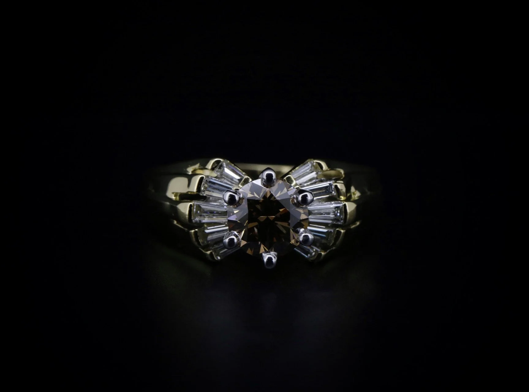 A gold and silver ring with a large central dark gemstone surrounded by smaller clear gemstones on a black background.