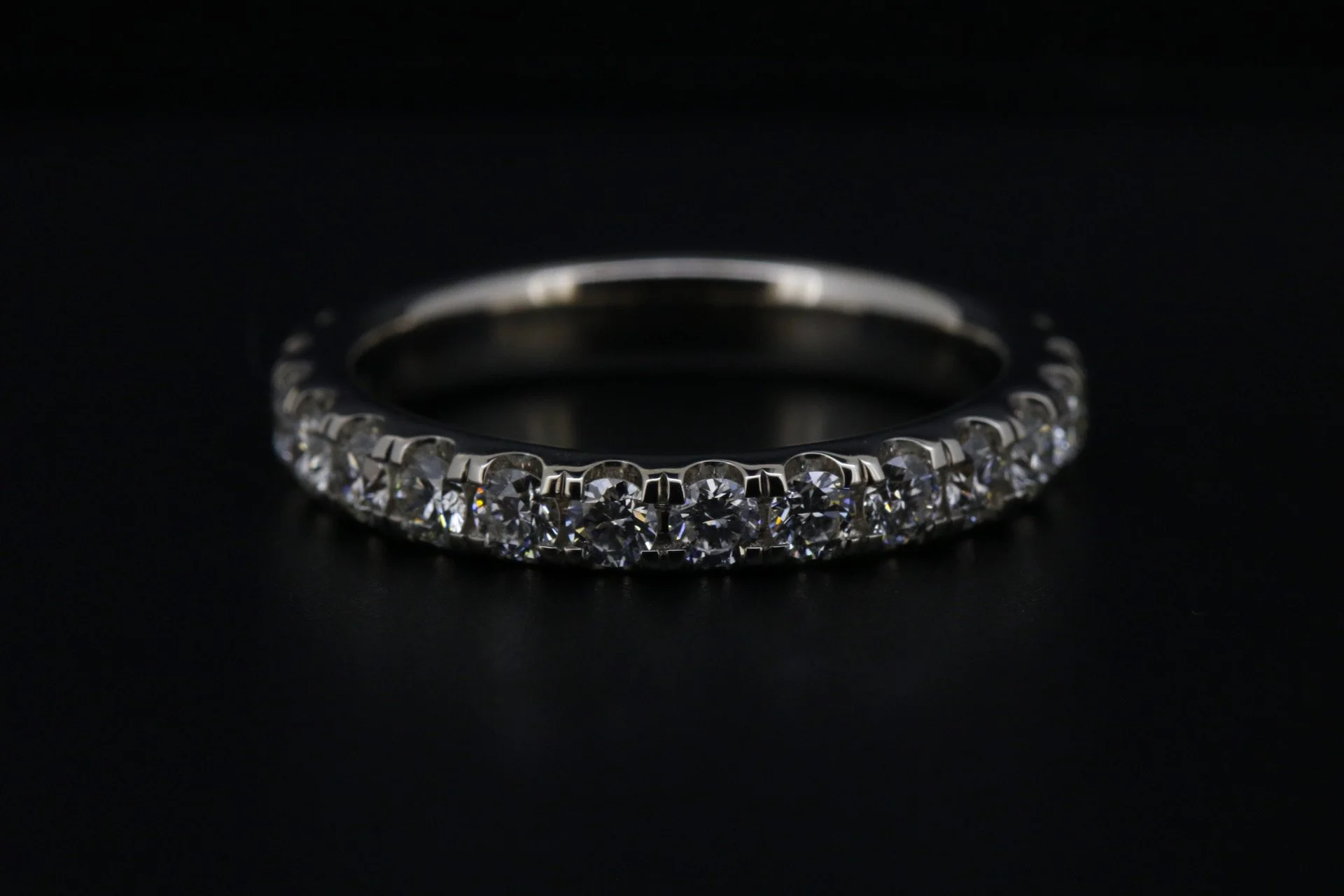 A silver ring with a row of clear, round-cut diamonds set around the band, displayed on a black surface.