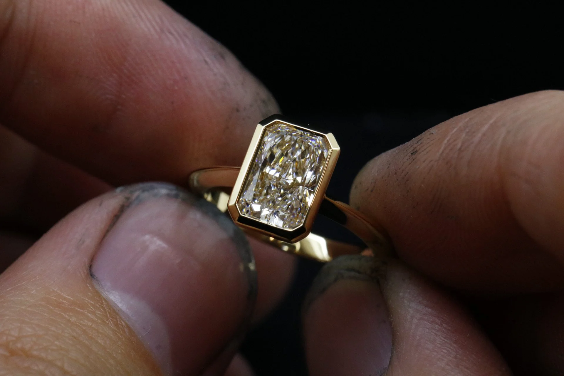 Close-up of a gold ring with a rectangular, emerald-cut diamond setting, held between fingers.