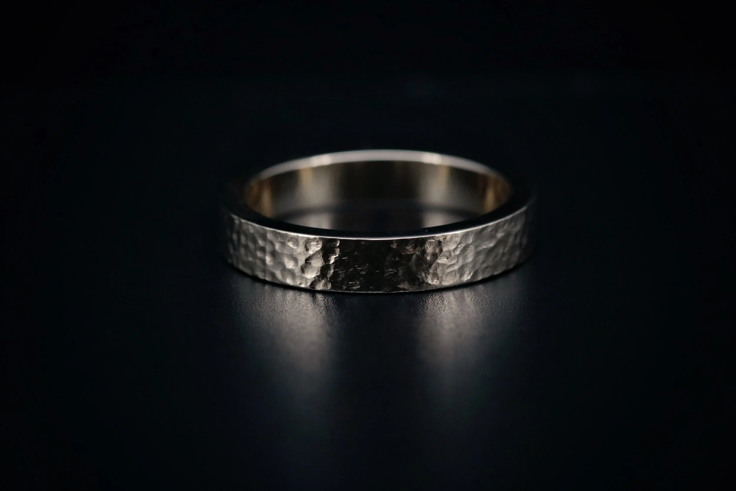 Silver textured wedding band on a dark surface.