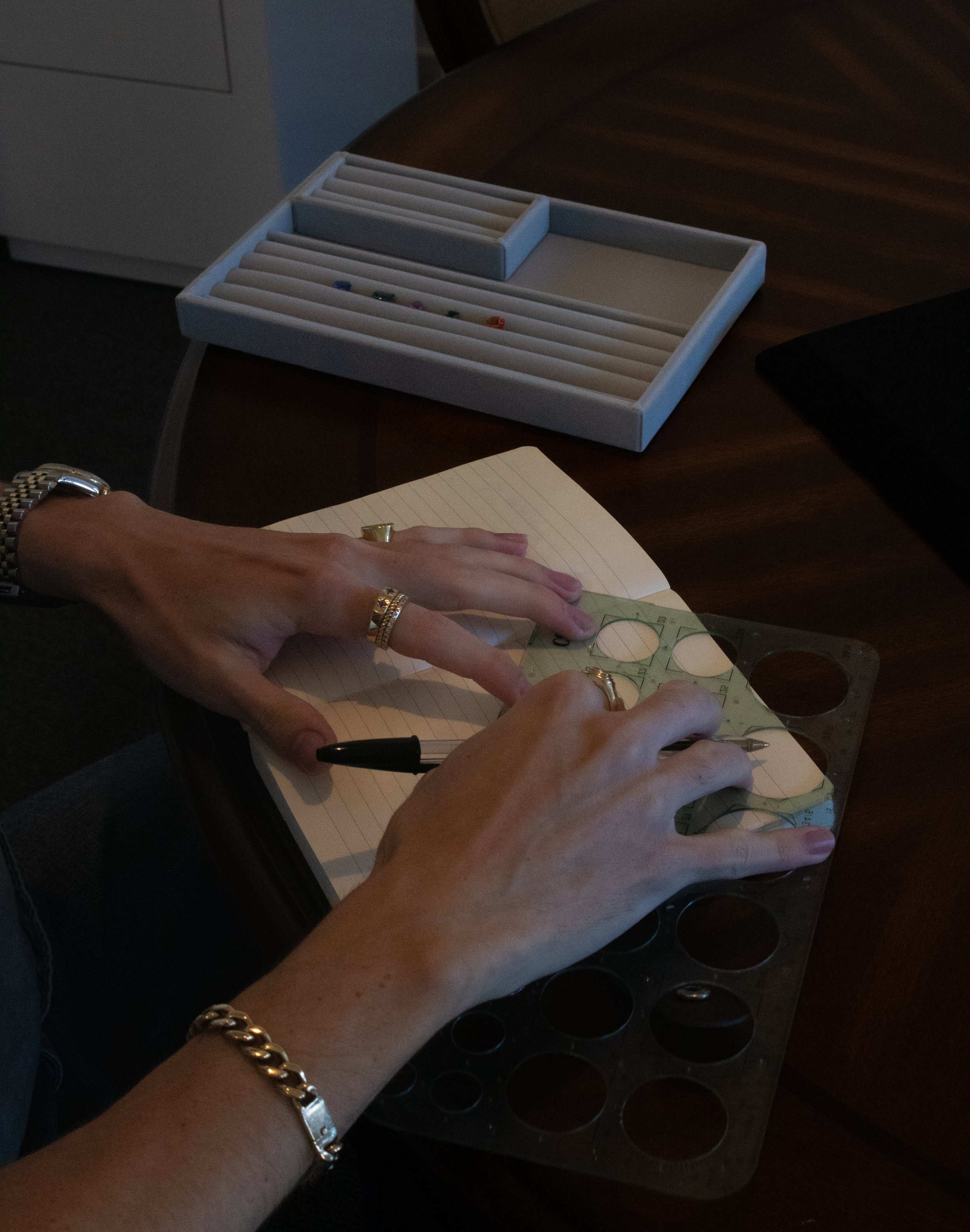 A person using a mechanical drawing template and pen at a desk, with a notepad and drafting tools nearby.