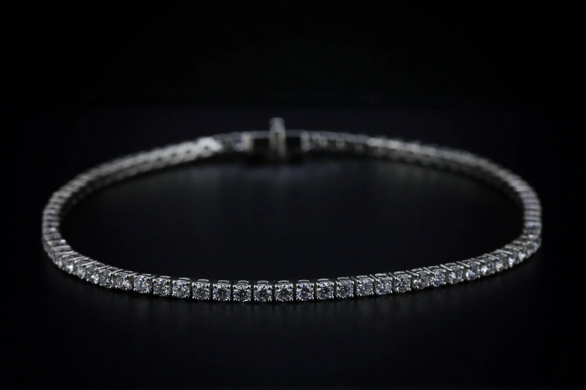 A diamond tennis bracelet on a black surface.