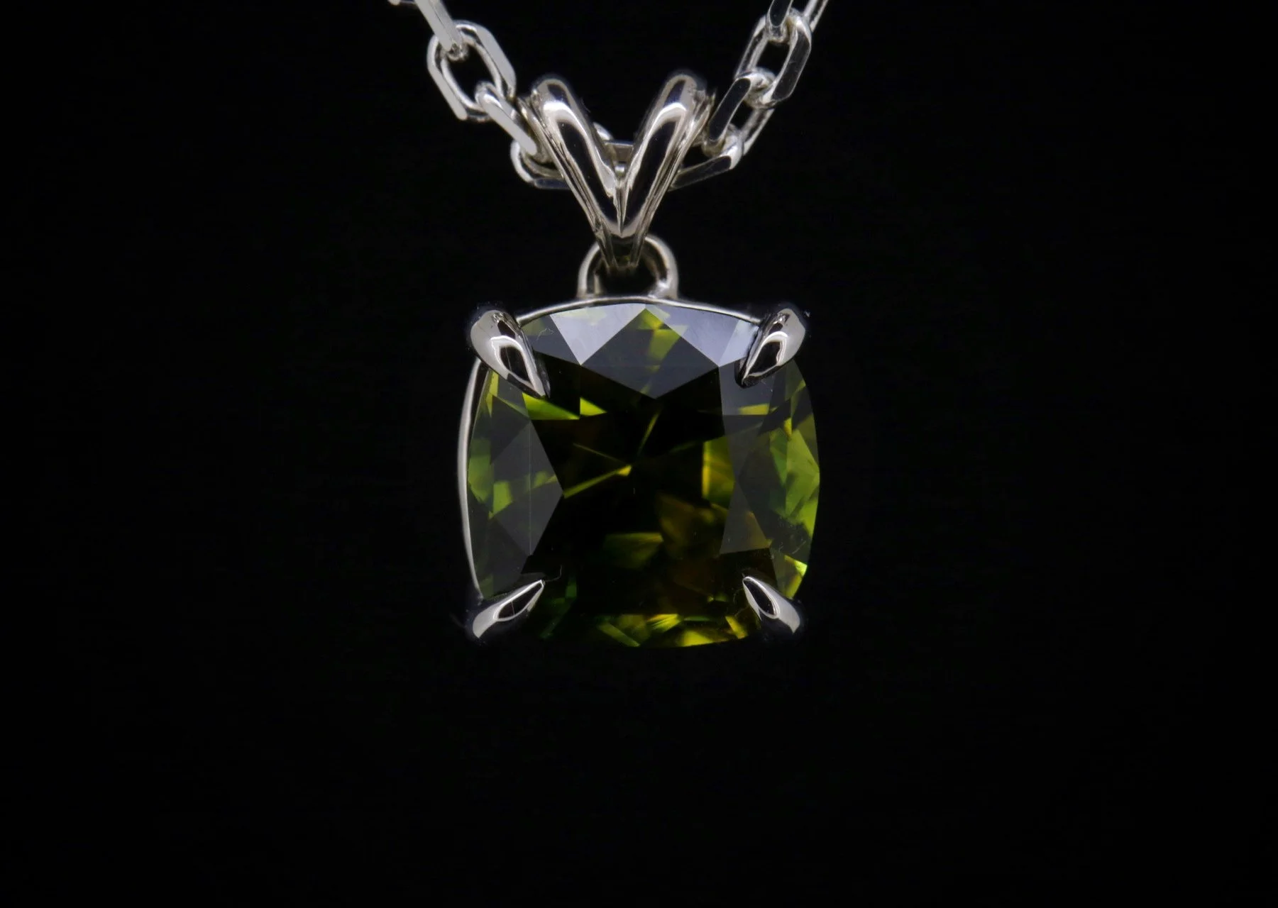 A close-up of a silver necklace with a large, rectangular, green gemstone pendant against a black background.