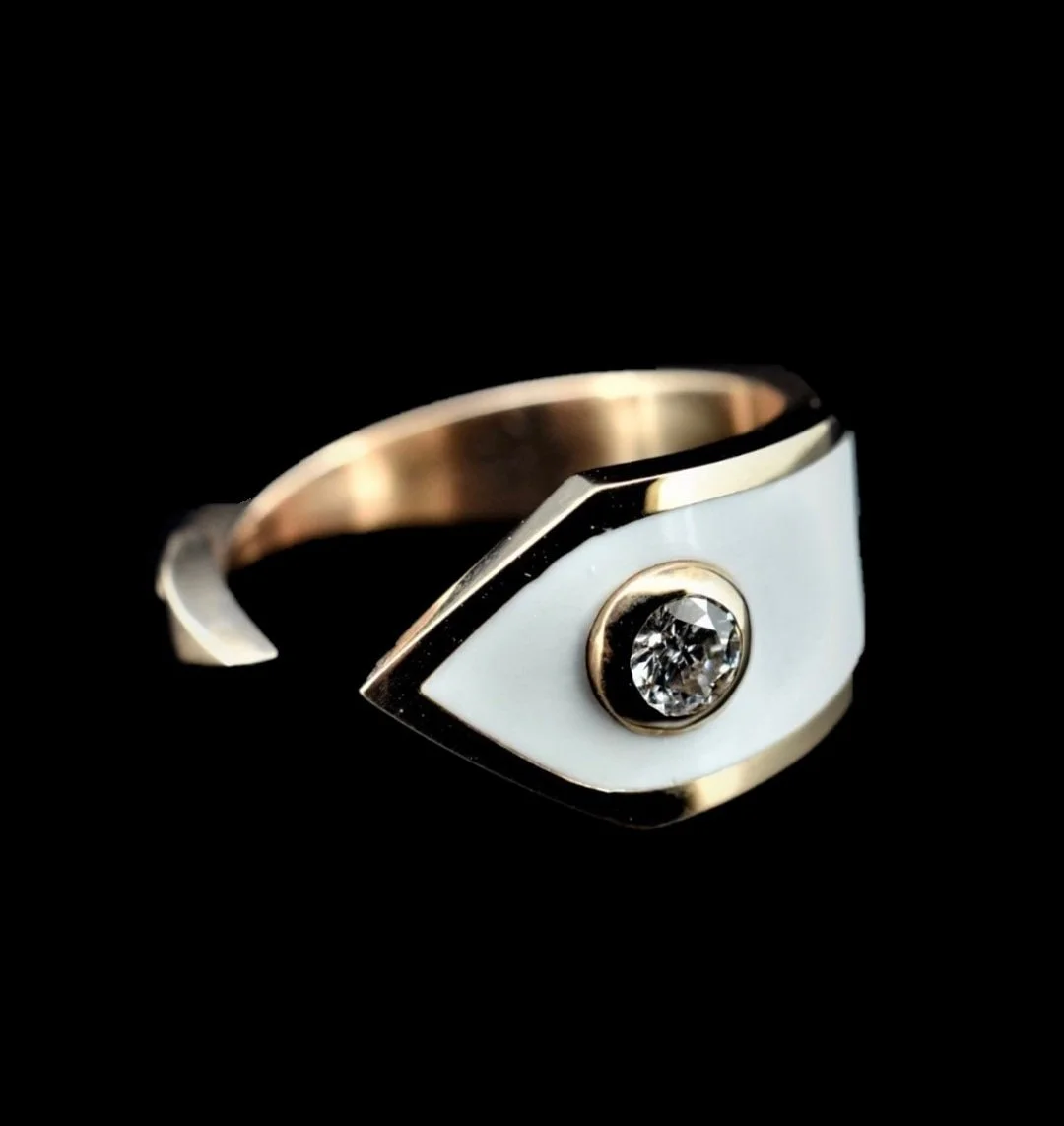 A gold ring with an eye-shaped white enamel design and a central diamond set in the middle of the eye.
