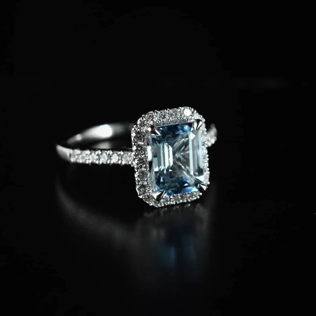 A silver ring with a large rectangular blue gemstone surrounded by small diamonds on a black background.