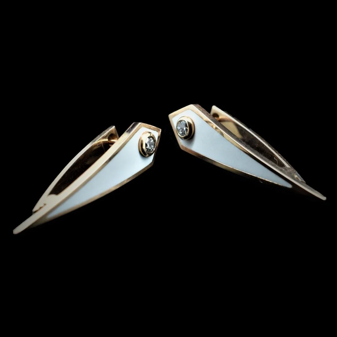 Pair of white and gold earrings with clear gemstones on a black background.