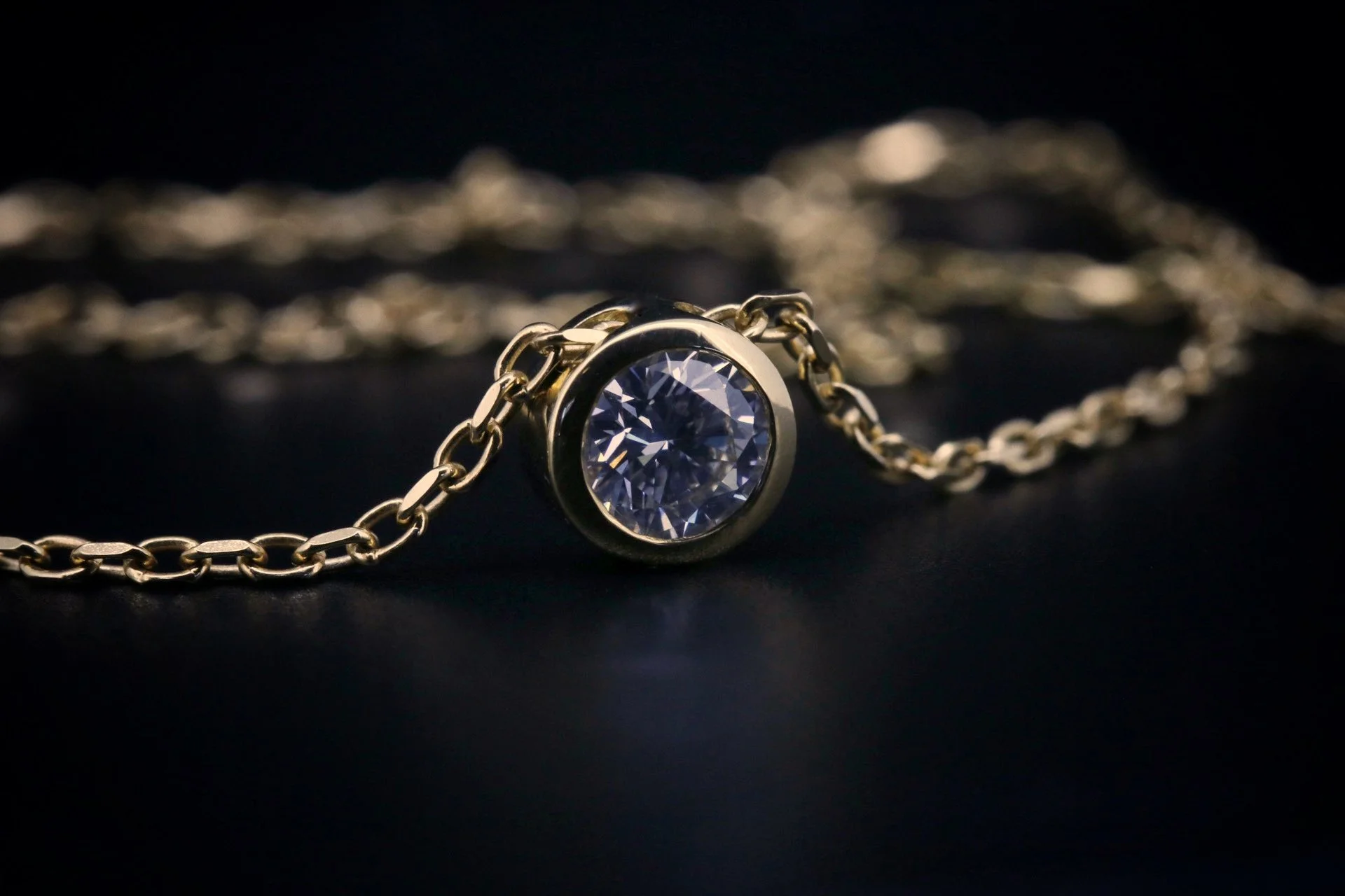 Gold chain necklace with a circular pendant featuring a large clear gemstone, against a dark background.