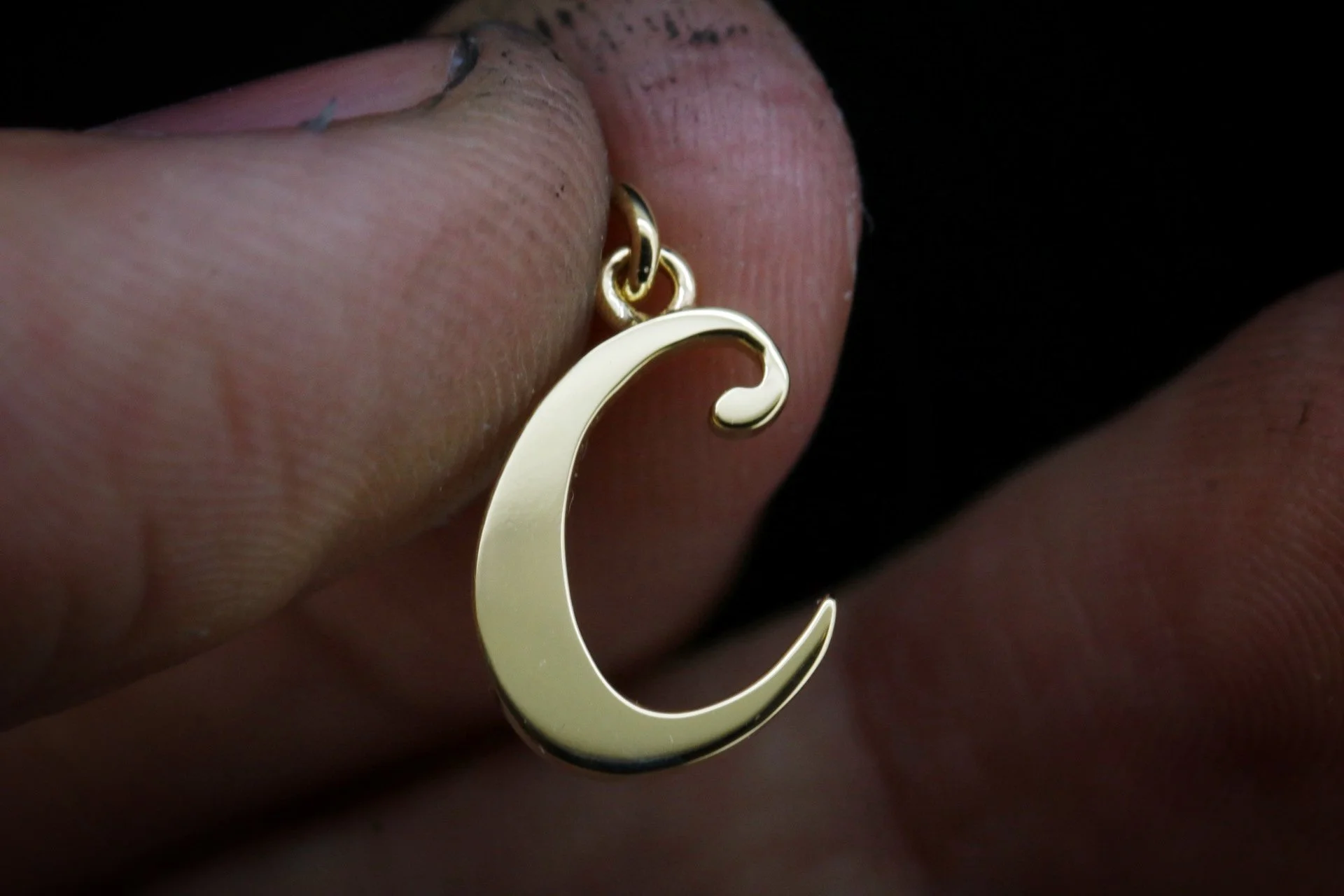 A hand holding a gold crescent moon-shaped earring against a dark background.