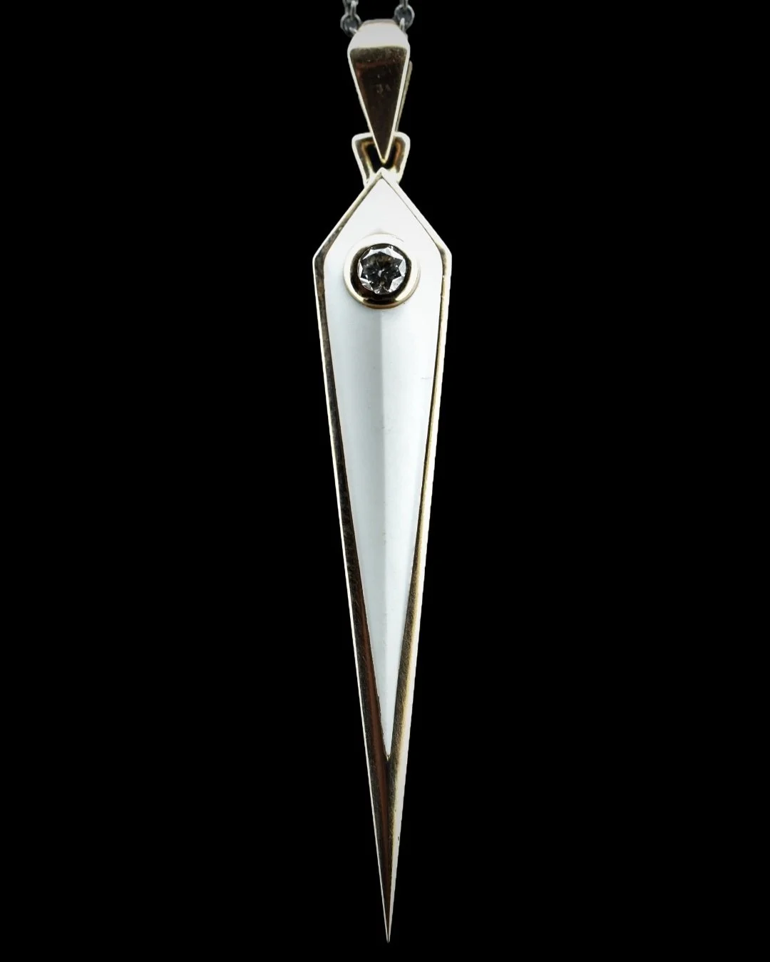 A close-up of a pendant with a white elongated triangular shape, a small black gemstone near the top, and a metallic frame, hanging against a black background.