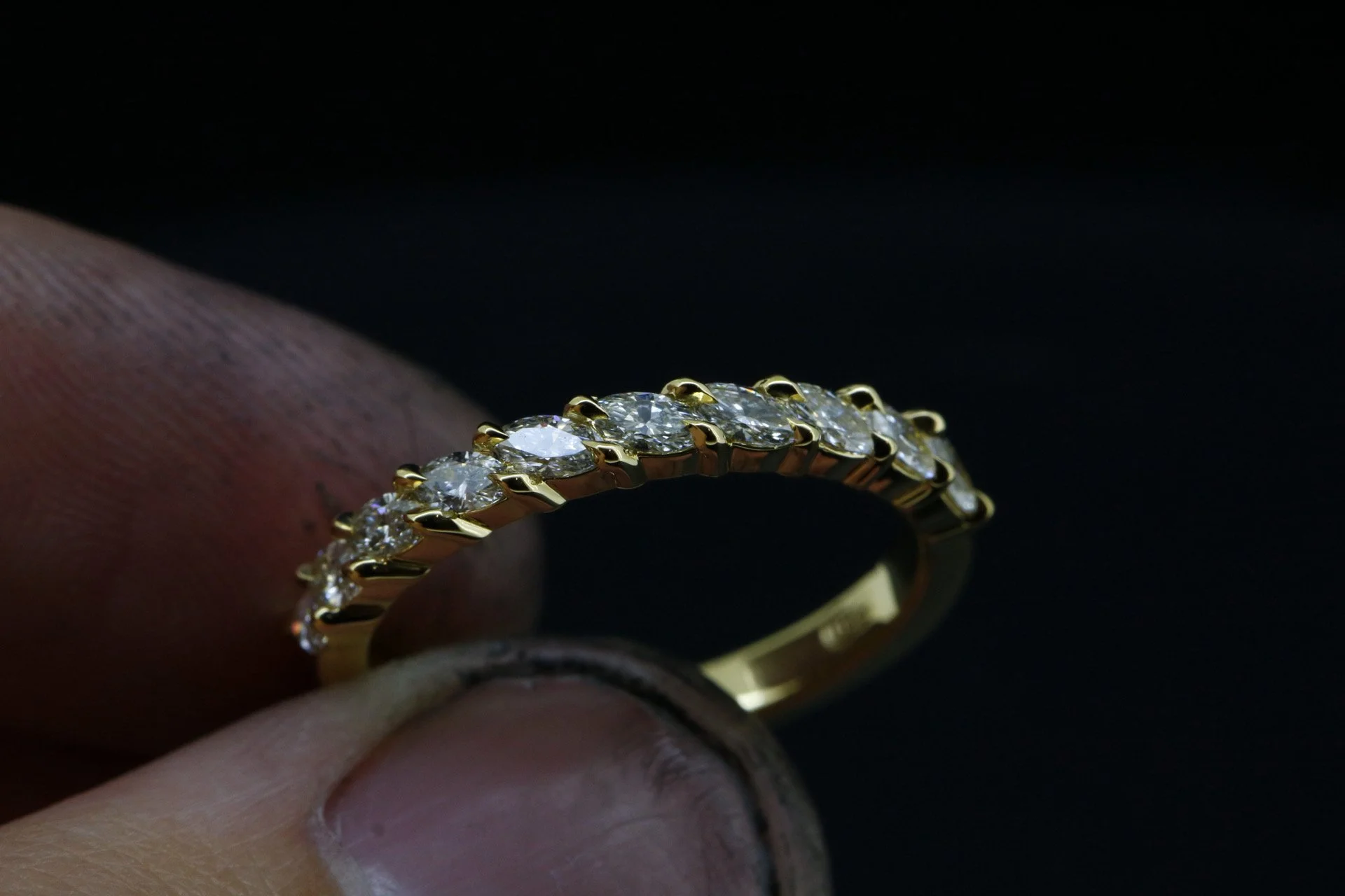 Close-up of a gold ring with multiple diamonds being held between fingers against a black background.