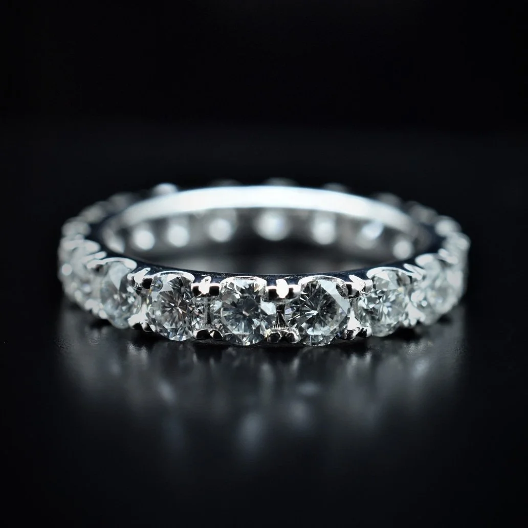 A close-up of a silver engagement ring with multiple round-cut diamonds set in a shared prong setting on a black background.