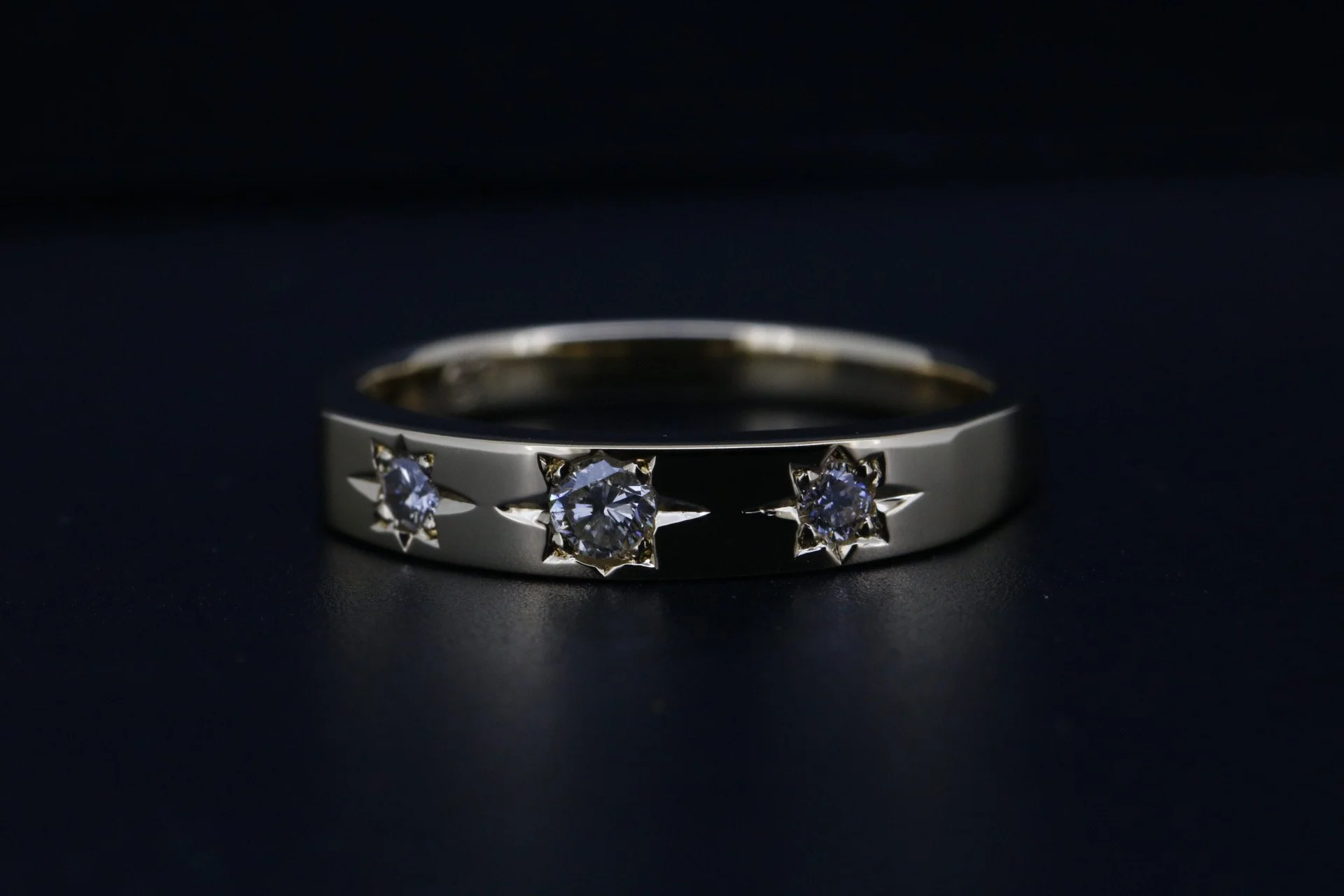 A silver ring with three evenly spaced diamonds set in star-shaped settings, resting on a dark surface.
