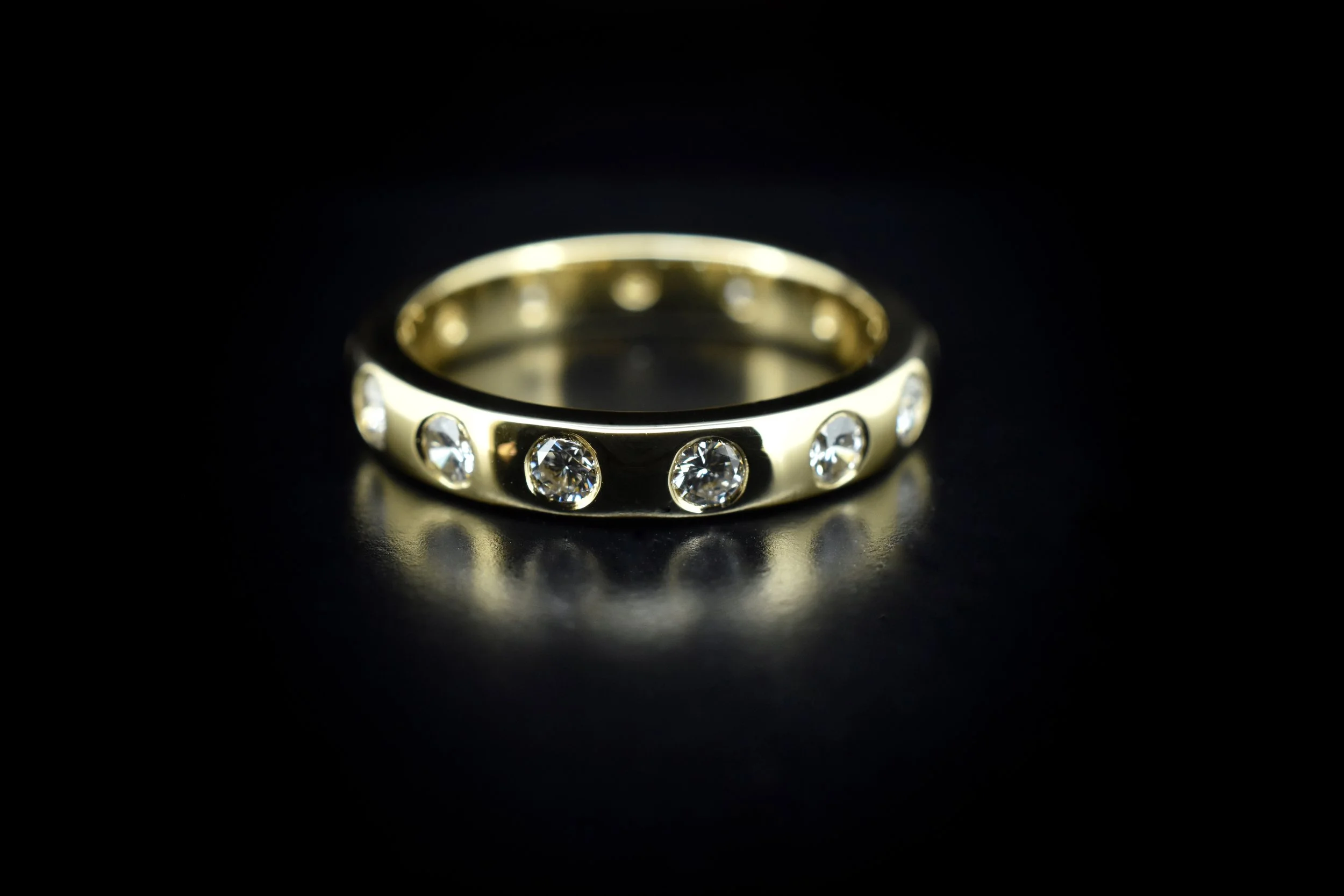 Gold ring with round diamonds embedded around its band, placed on a black surface with a reflective sheen.