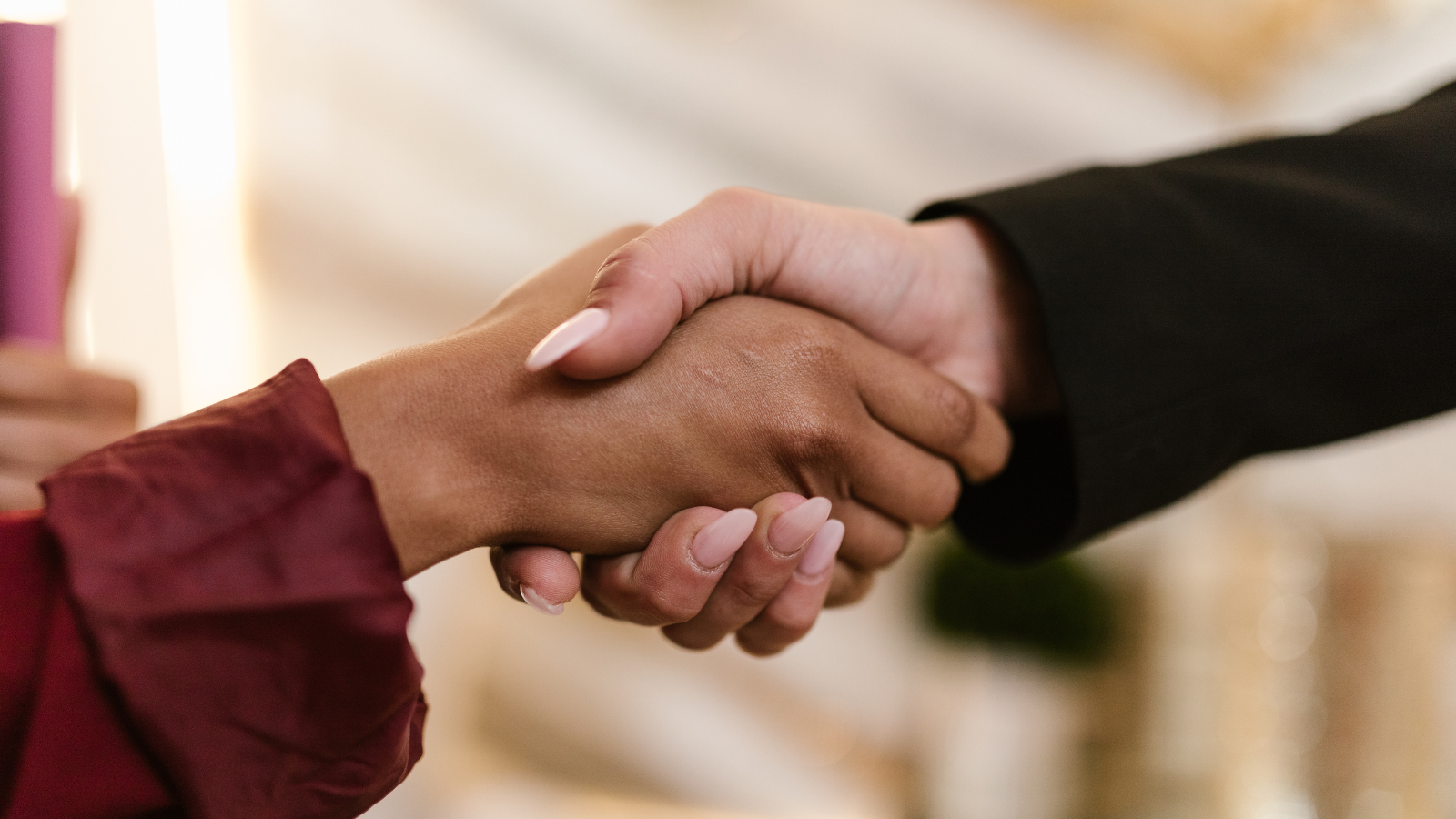 A close-up of two people shaking hands, one wearing a red sleeve and the other in a black sleeve.