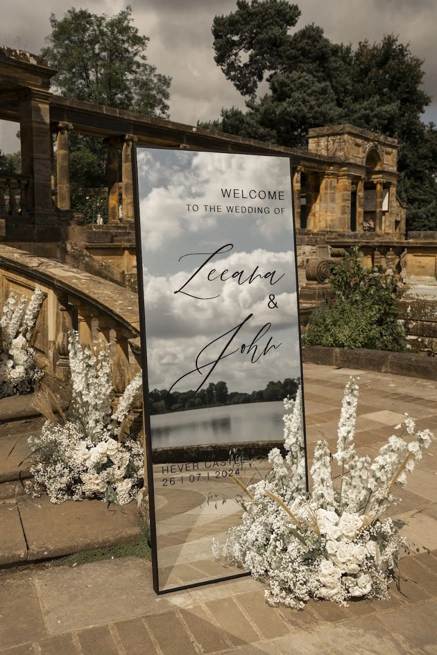Full-length mirrored wedding welcome sign with white floral arrangements at Hever Castle