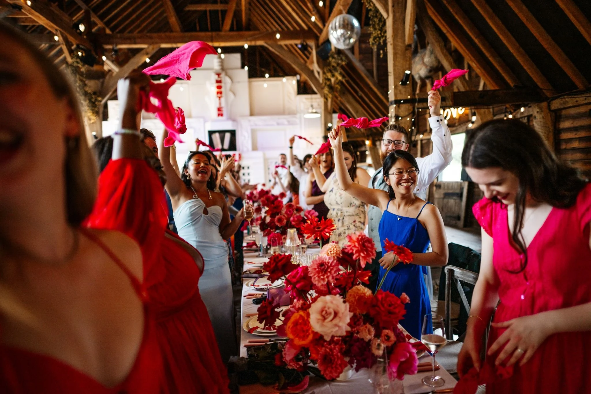 Wedding guests waving pink napkins above colourful floral reception tables at Preston Court
