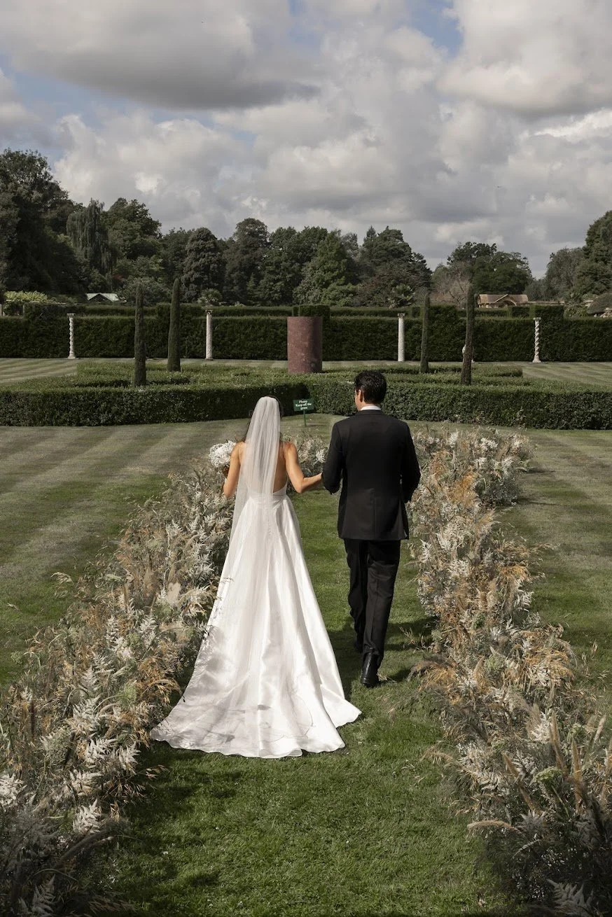 Bride and groom walking through a meadow-style wedding floral installation