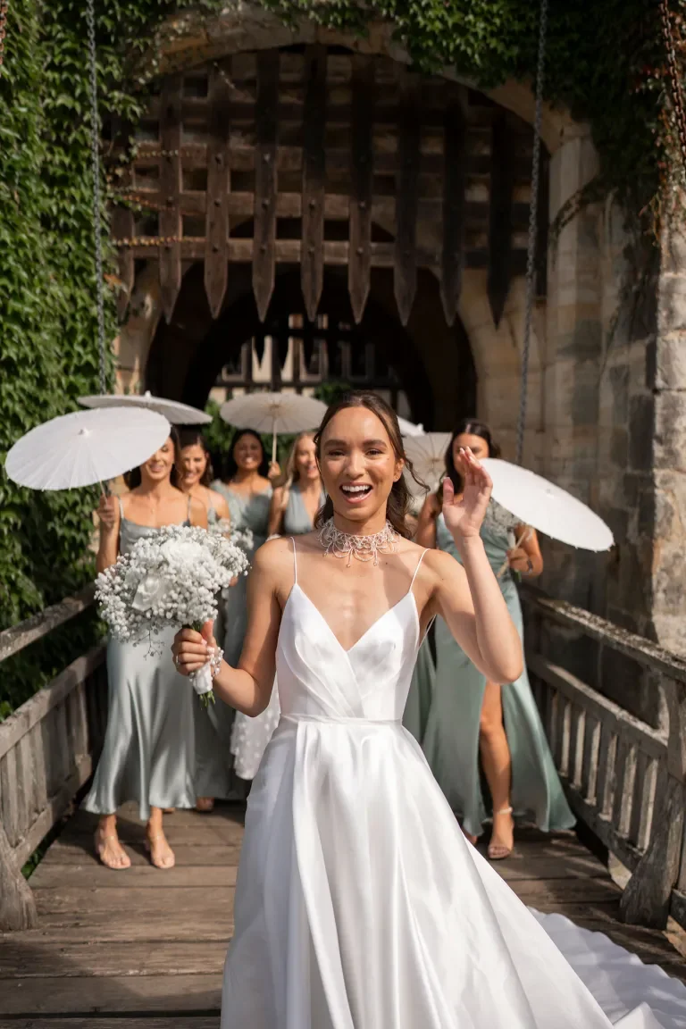 Bride and bridesmaids with white bouquets and parasols on the bridge at Hever Castle