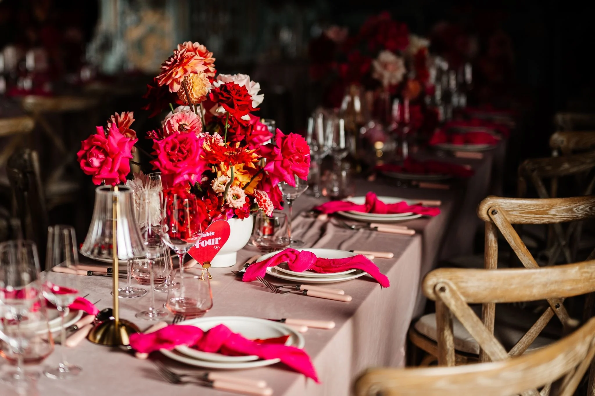 Pink, red and orange wedding flowers with pink napkins and heart table numbers at Preston Court