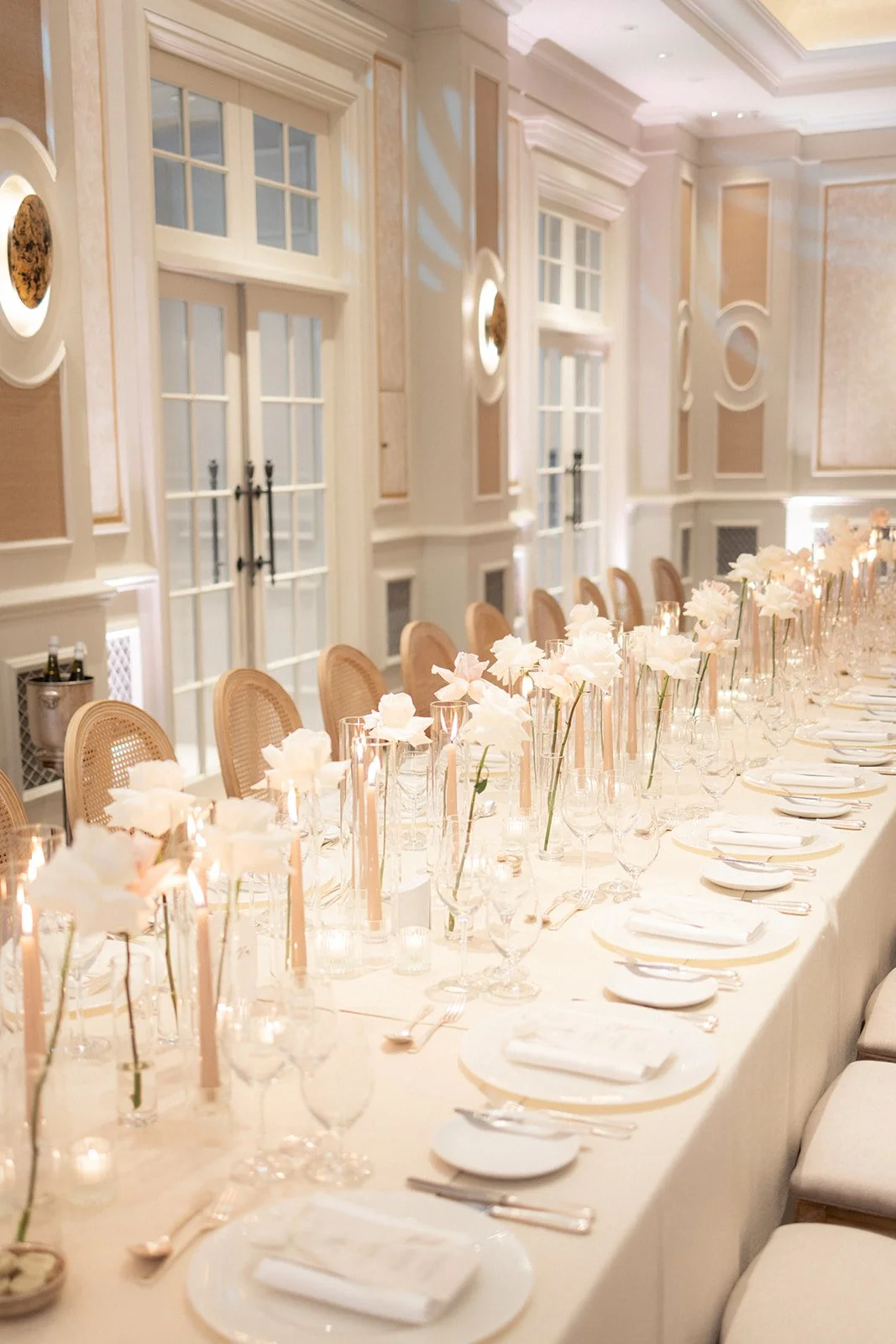 Elegant banquet table set with white flowers, candles, and fine china in a decorated banquet hall.