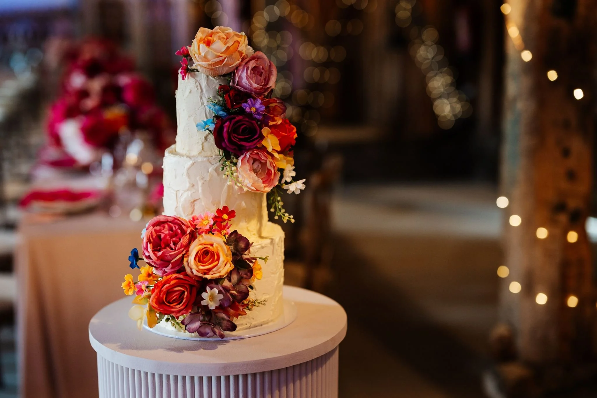Three-tier wedding cake decorated with colourful flowers on a fluted display plinth