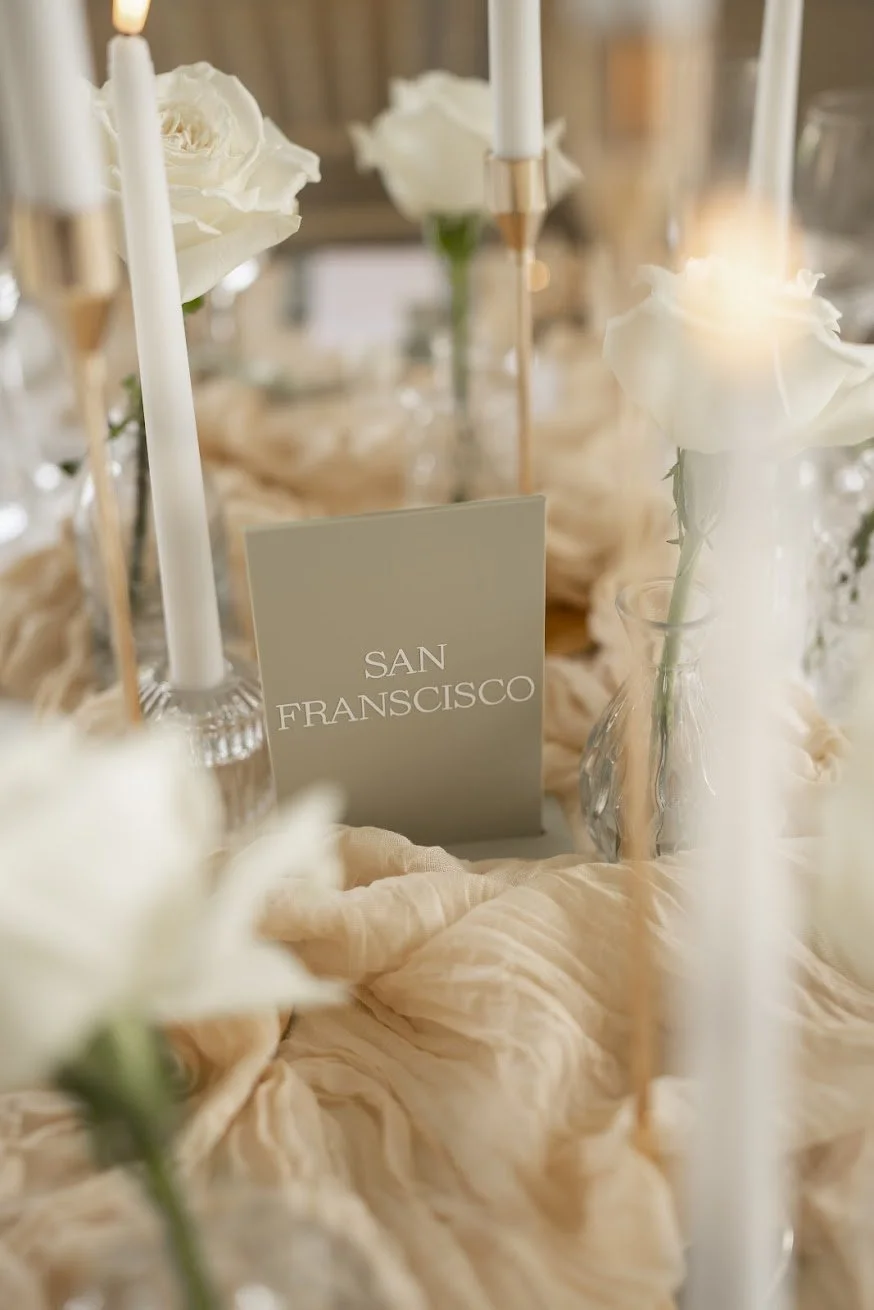 Minimal sage-green wedding table name cards with white flowers and neutral fabric