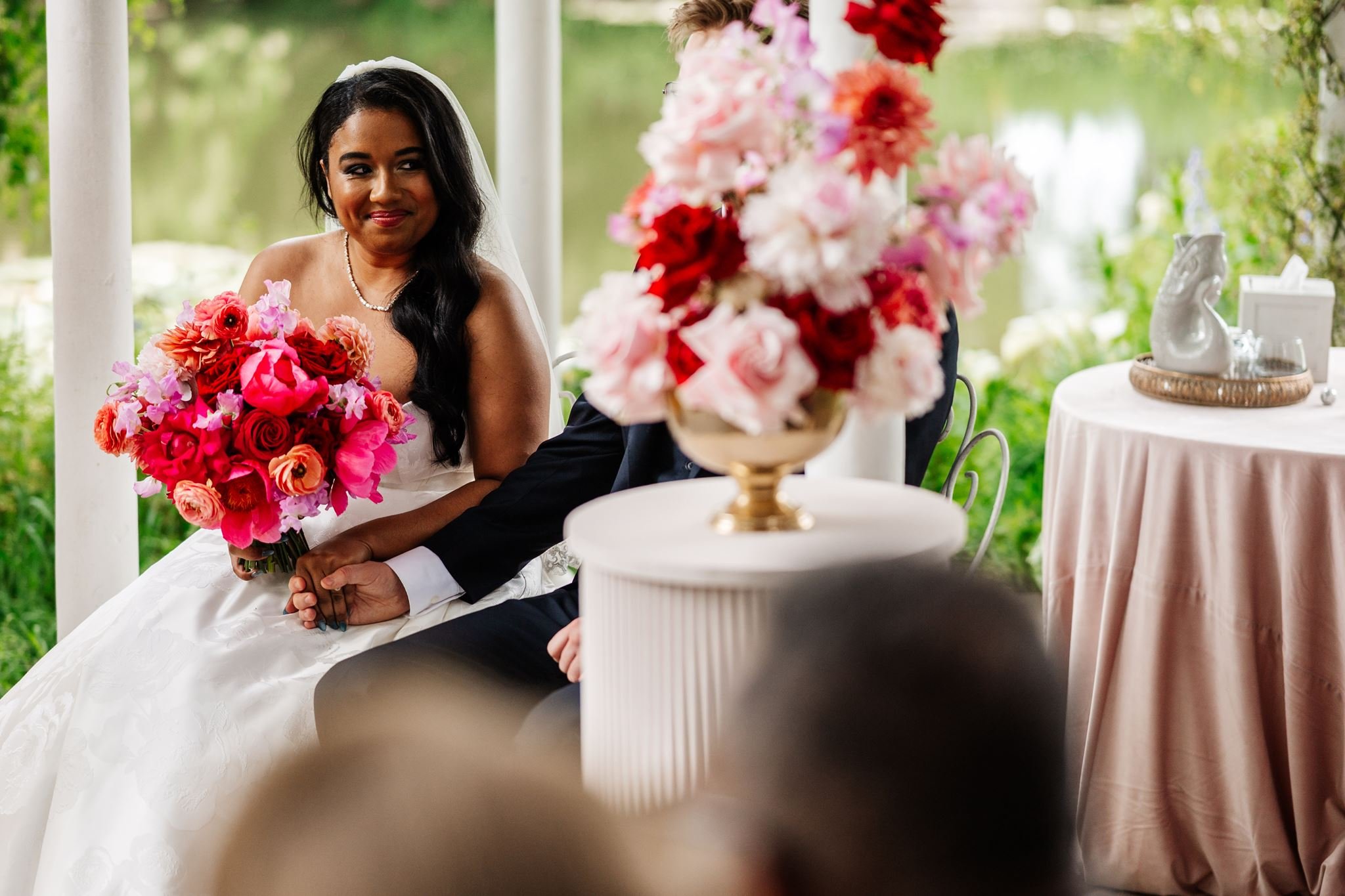 Diana holding a vibrant pink and red bridal bouquet beside the ceremony flowers at Preston Court