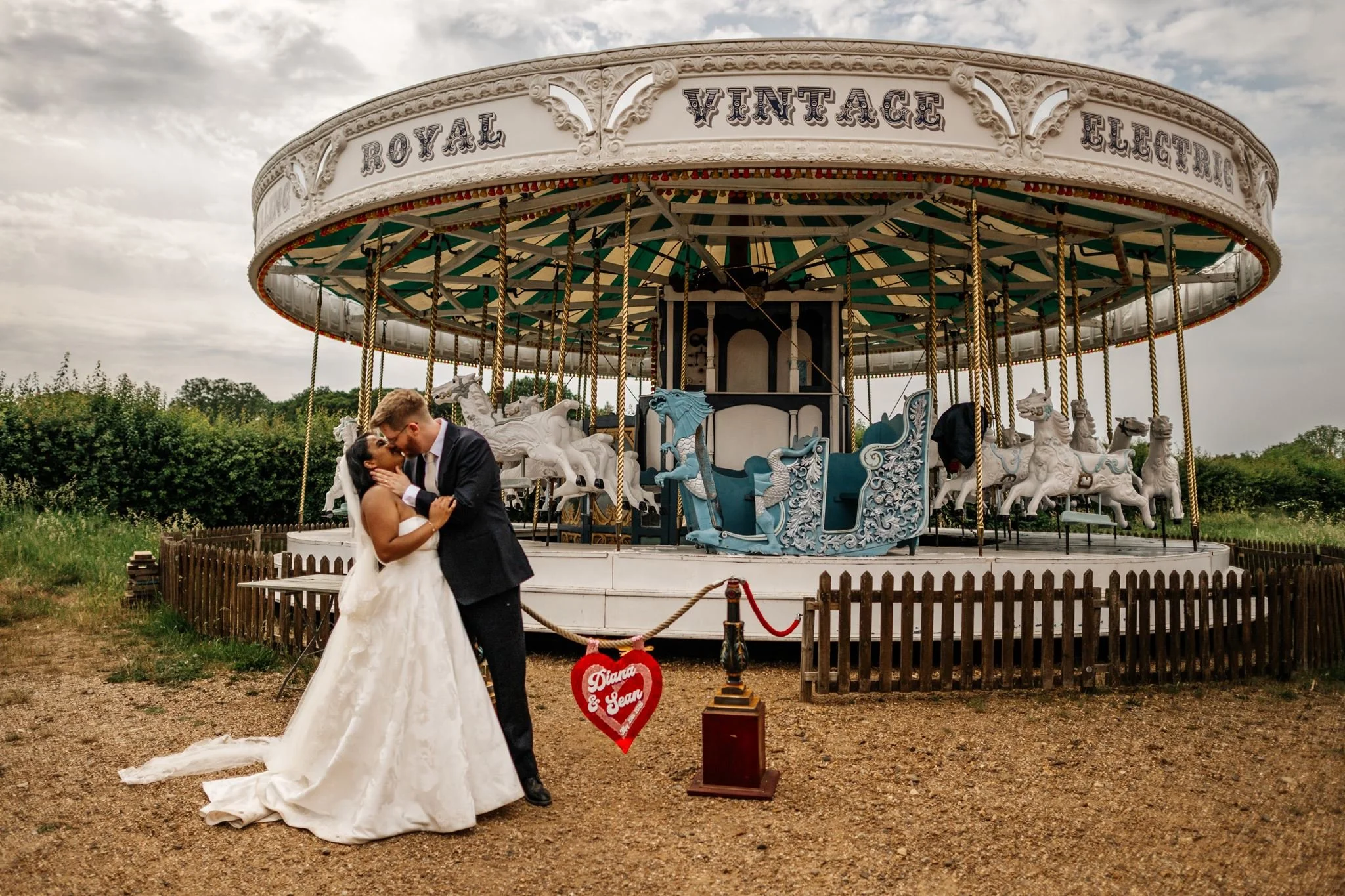 Diana and Sean kissing beside Preston Court’s vintage carousel and their personalised heart sign