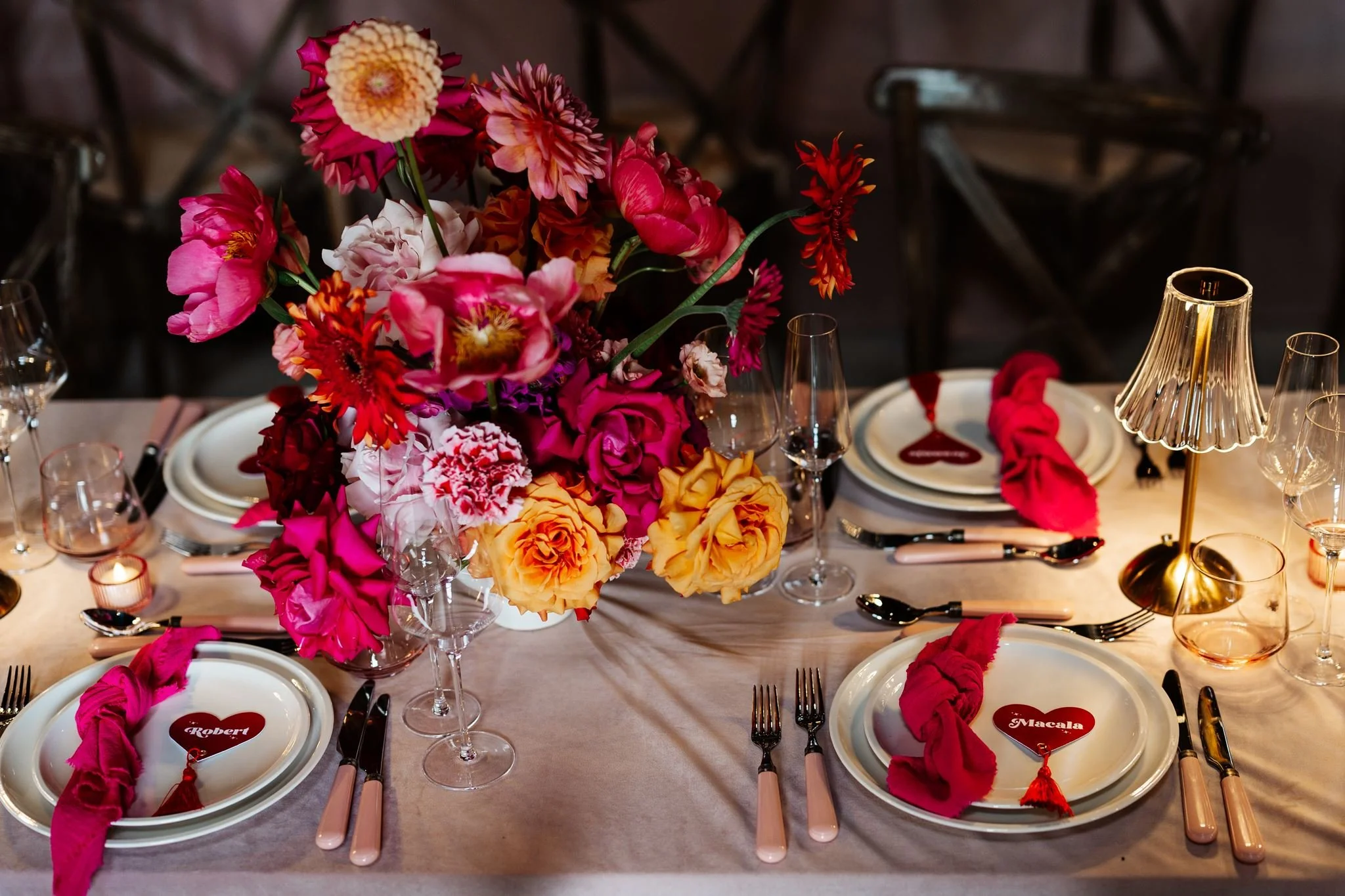 Overhead view of colourful wedding flowers, pink napkins, heart place names and a gold table lamp