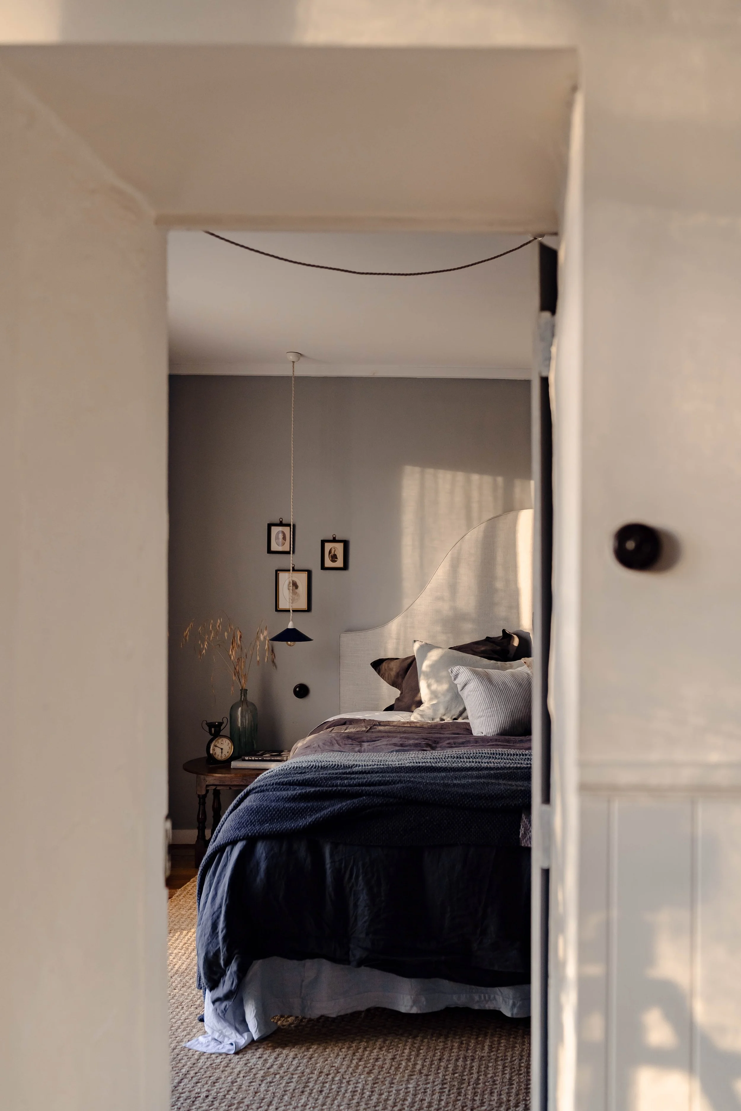 A mirror reflecting a cozy bedroom with a bed, pillows, and a nightstand with a clock and vase.