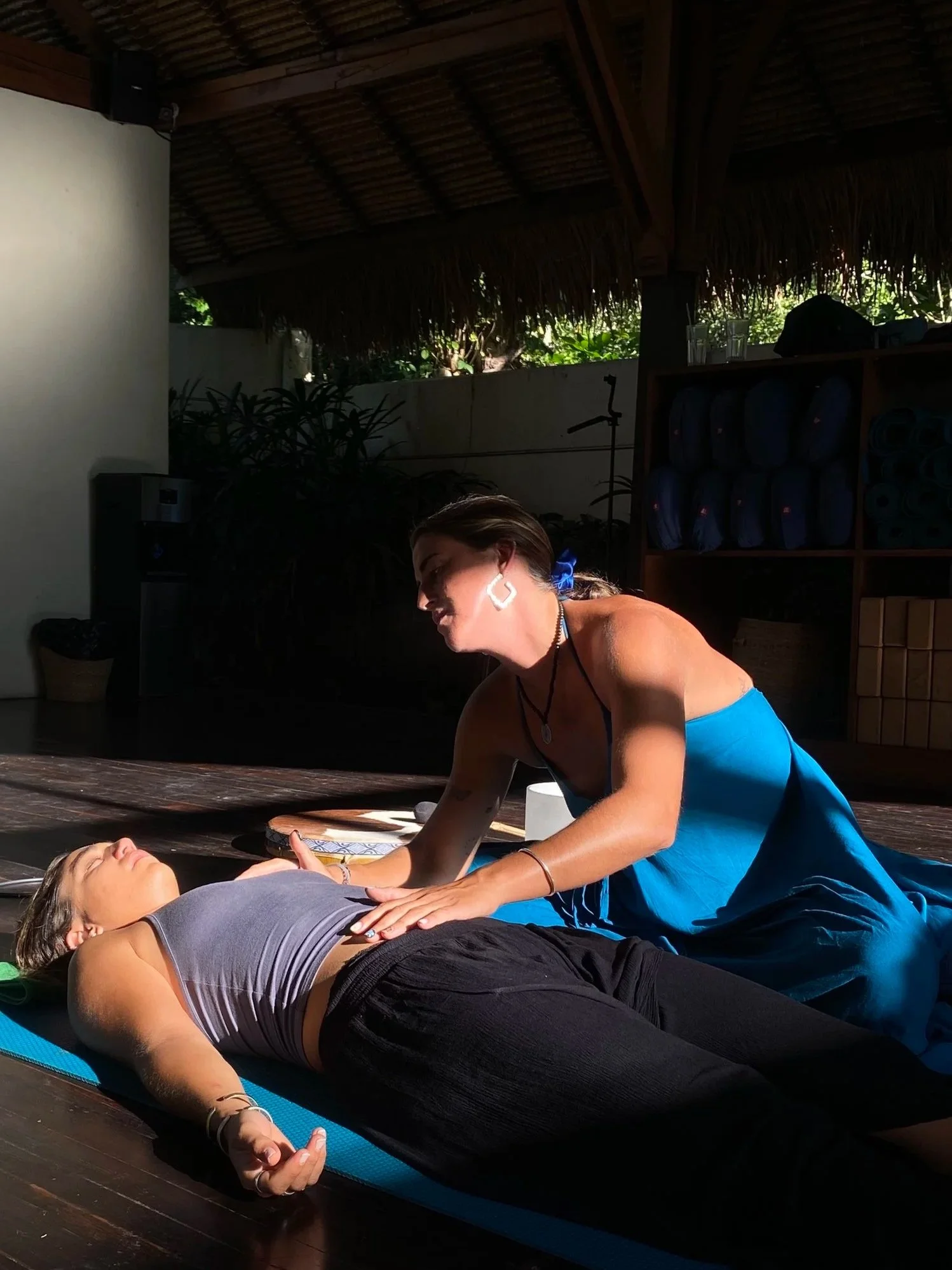 Mujer dando una sesión de yoga o meditación a otra mujer en un espacio de interior con iluminación natural.
