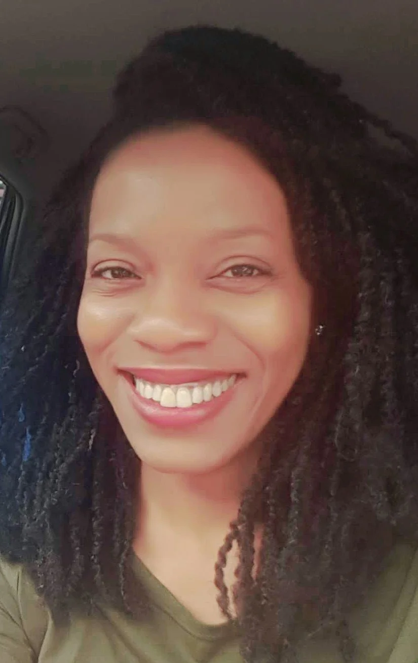 Close-up photo of smiling woman with natural curly hair, wearing a green top, inside a vehicle.