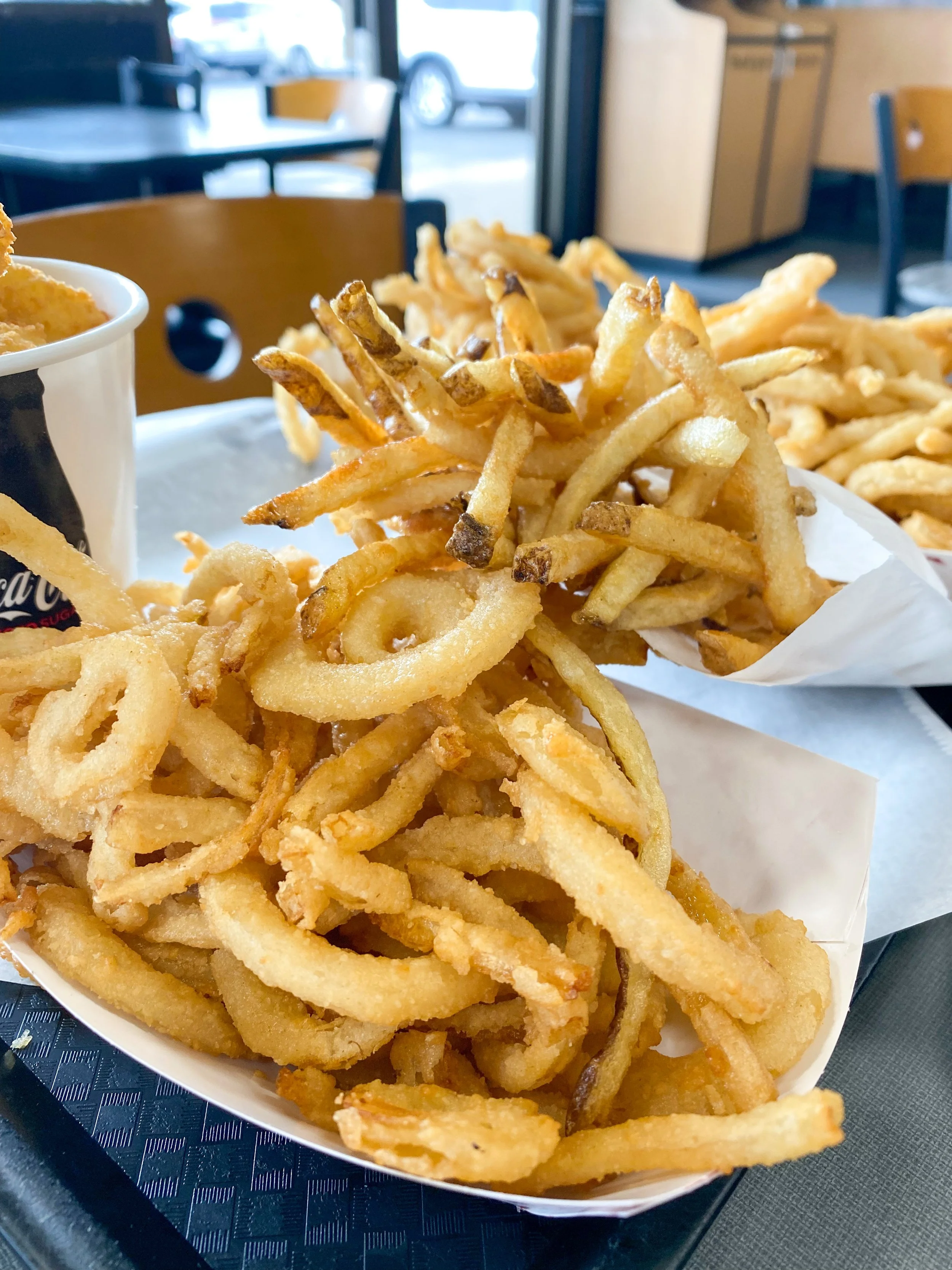 Basket of fried onion rings and French fries on a tray inside a restaurant.