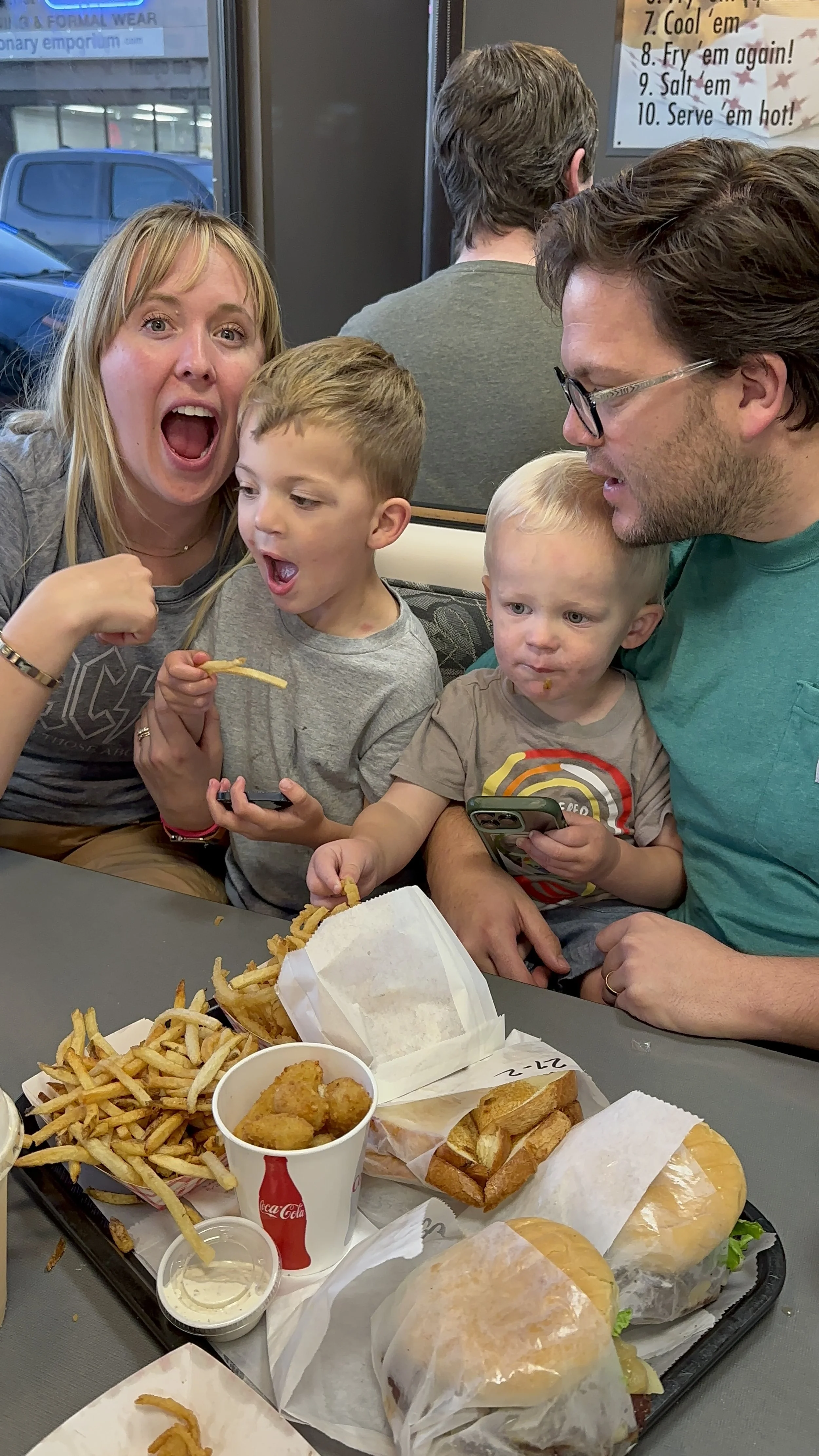 A woman and a man with two young boys at a fast-food restaurant, celebrating and enjoying chicken nuggets, fries, and sandwiches.
