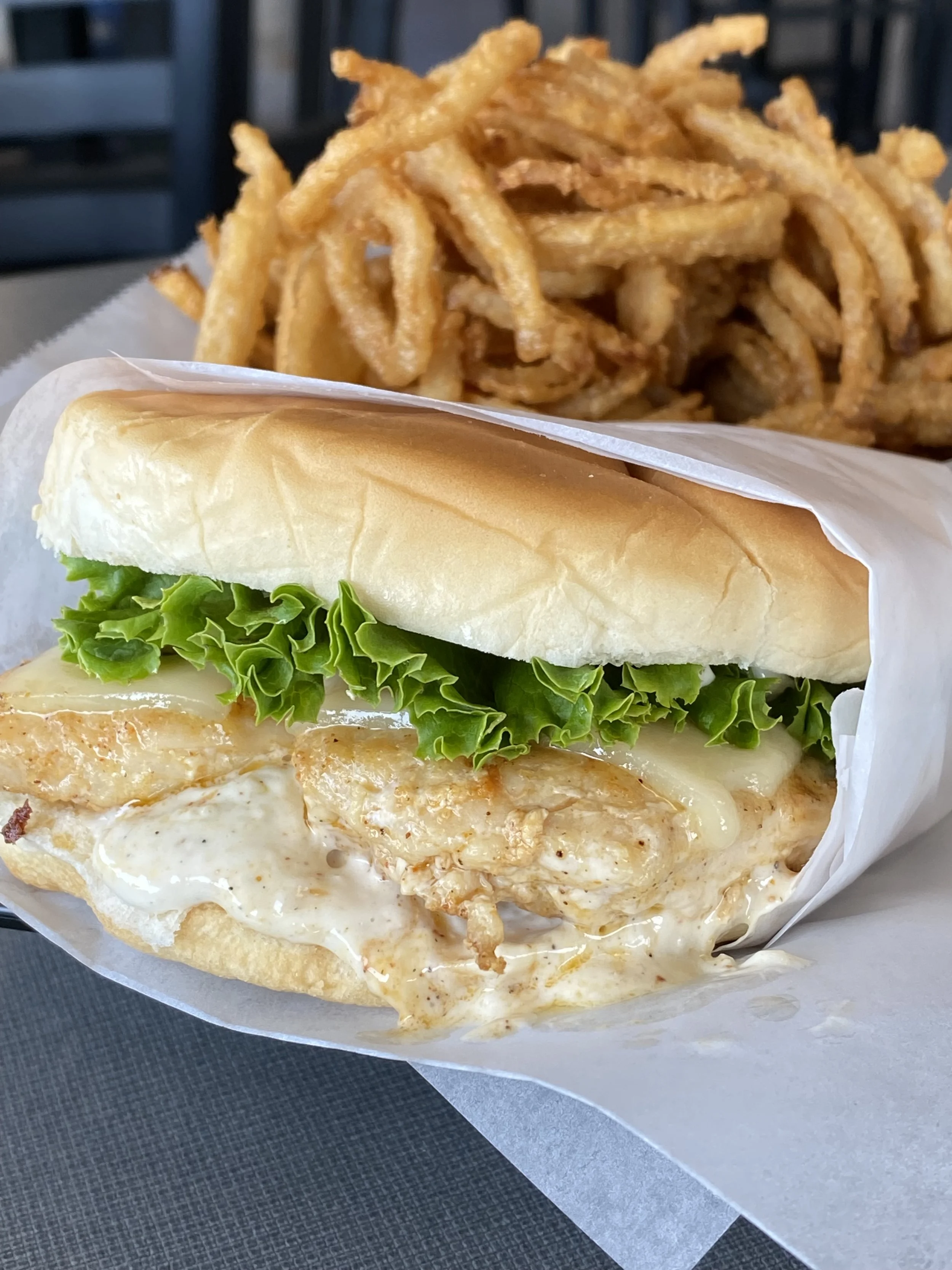 Fried chicken sandwich with lettuce and melted cheese, served with a side of fried onion rings.