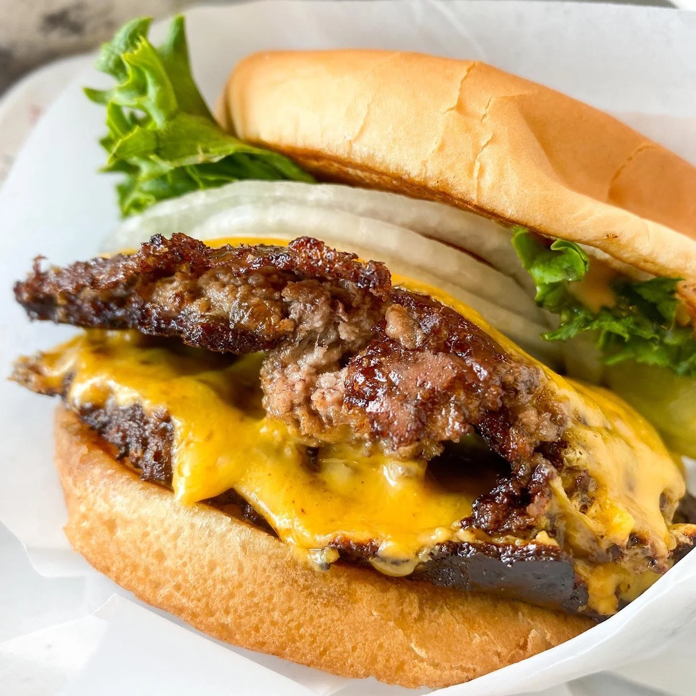 Close-up of a cheeseburger with a beef patty, melted cheddar cheese, lettuce, and onions in a soft bun.
