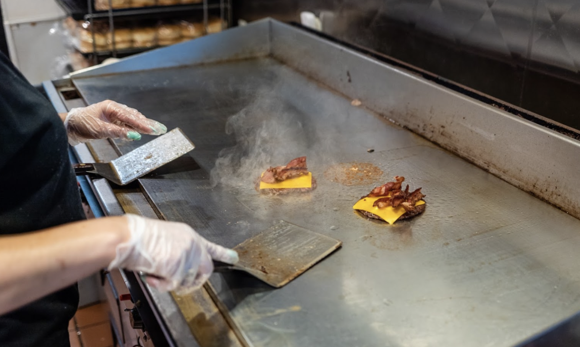 Person cooking bacon and cheese on a flat-top grill.