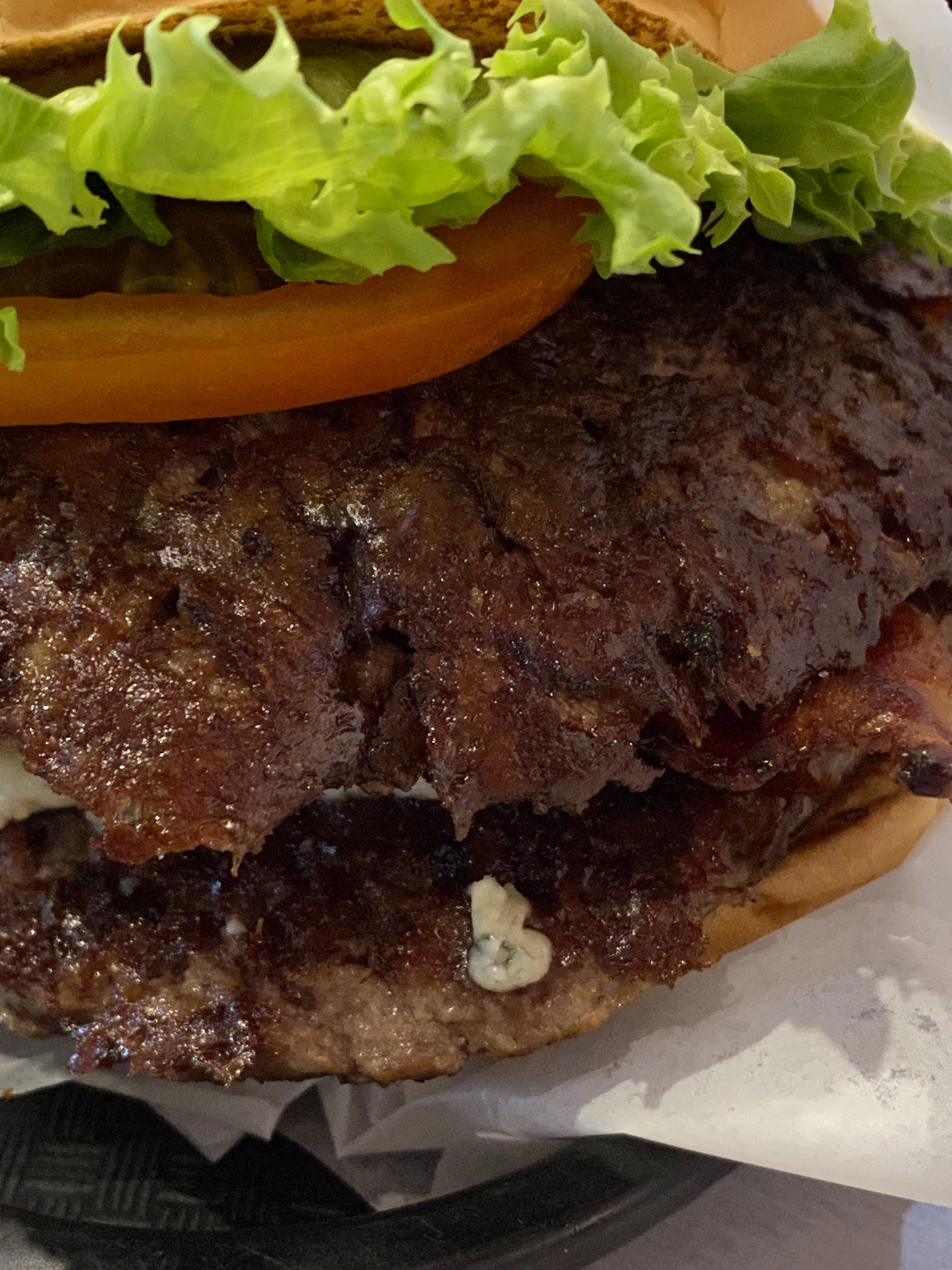 Close-up of a burger with lettuce, tomato, grilled meat patty, and some cheese, served in a basket with wrapping paper.