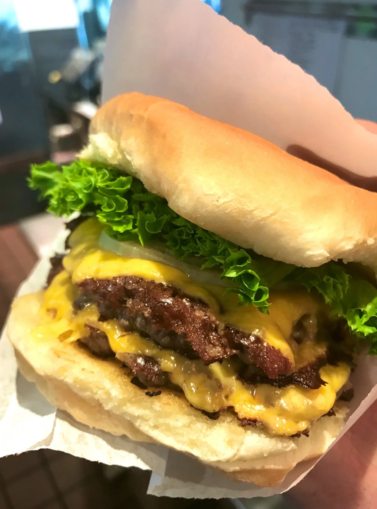 Close-up of a cheeseburger with lettuce, pickles, cheese, bacon, and a bun, held in a hand.