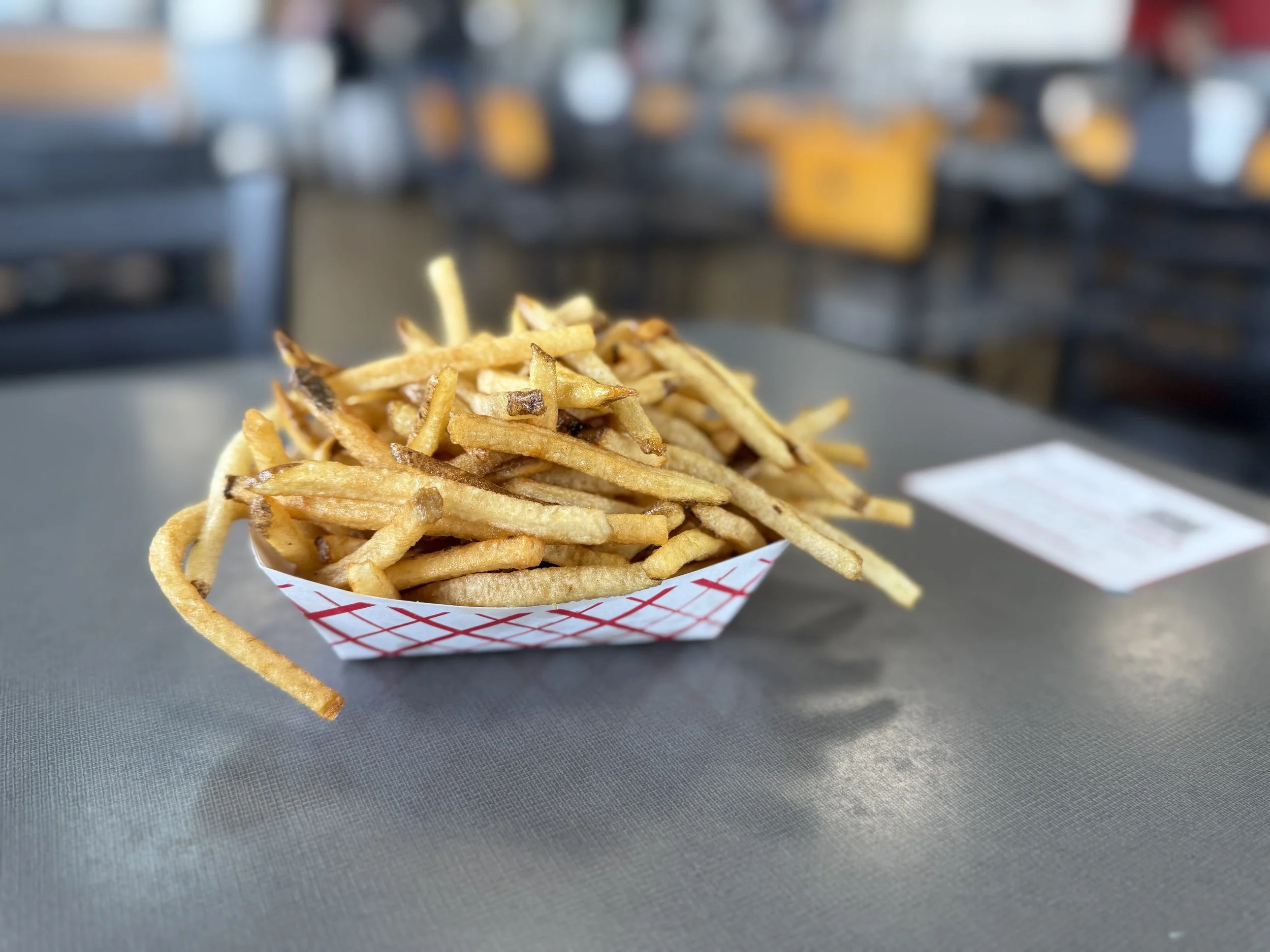 A serving of French fries in a paper tray on a gray table in a restaurant.